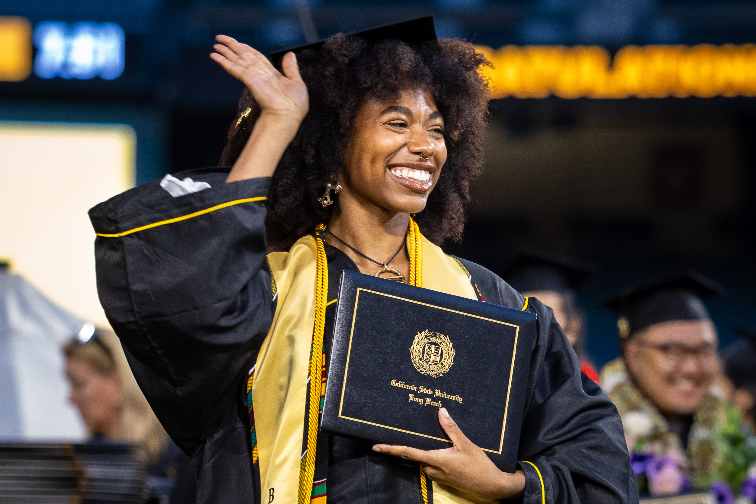 A CSULB grad waving and holding her diploma cover