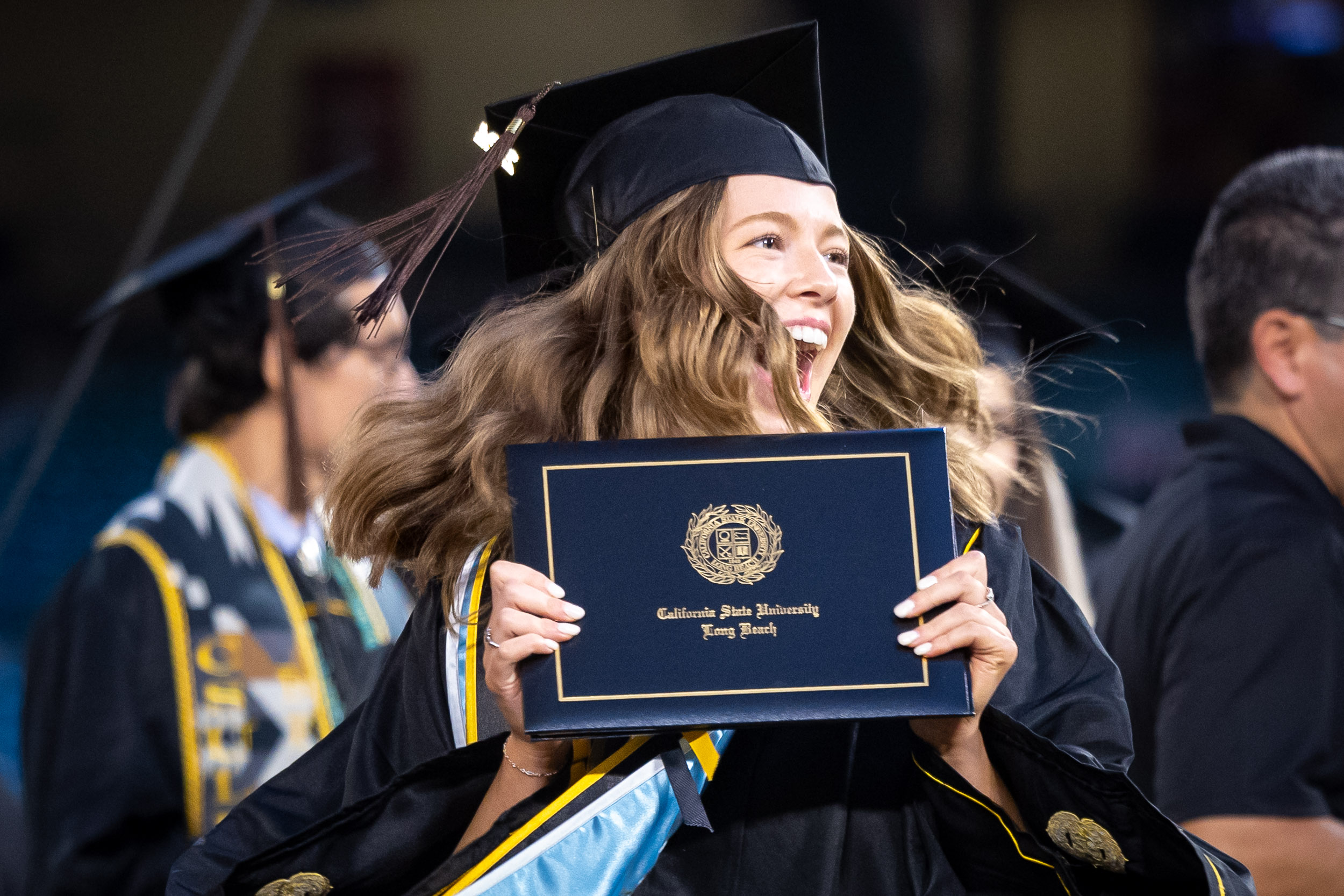 An excited CSULB grad holding her diploma cover