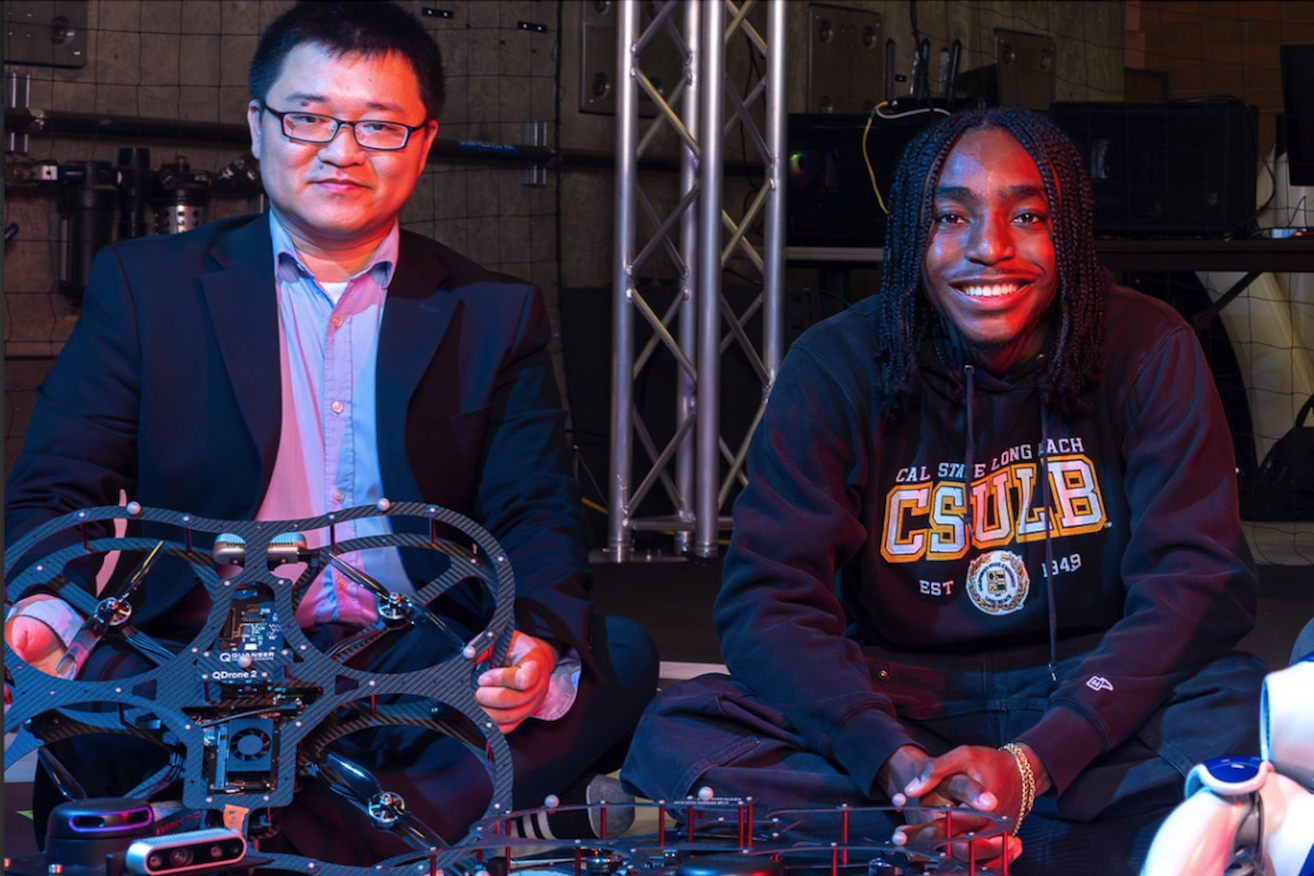 Two people sit in a dark room with one of them holding a drone