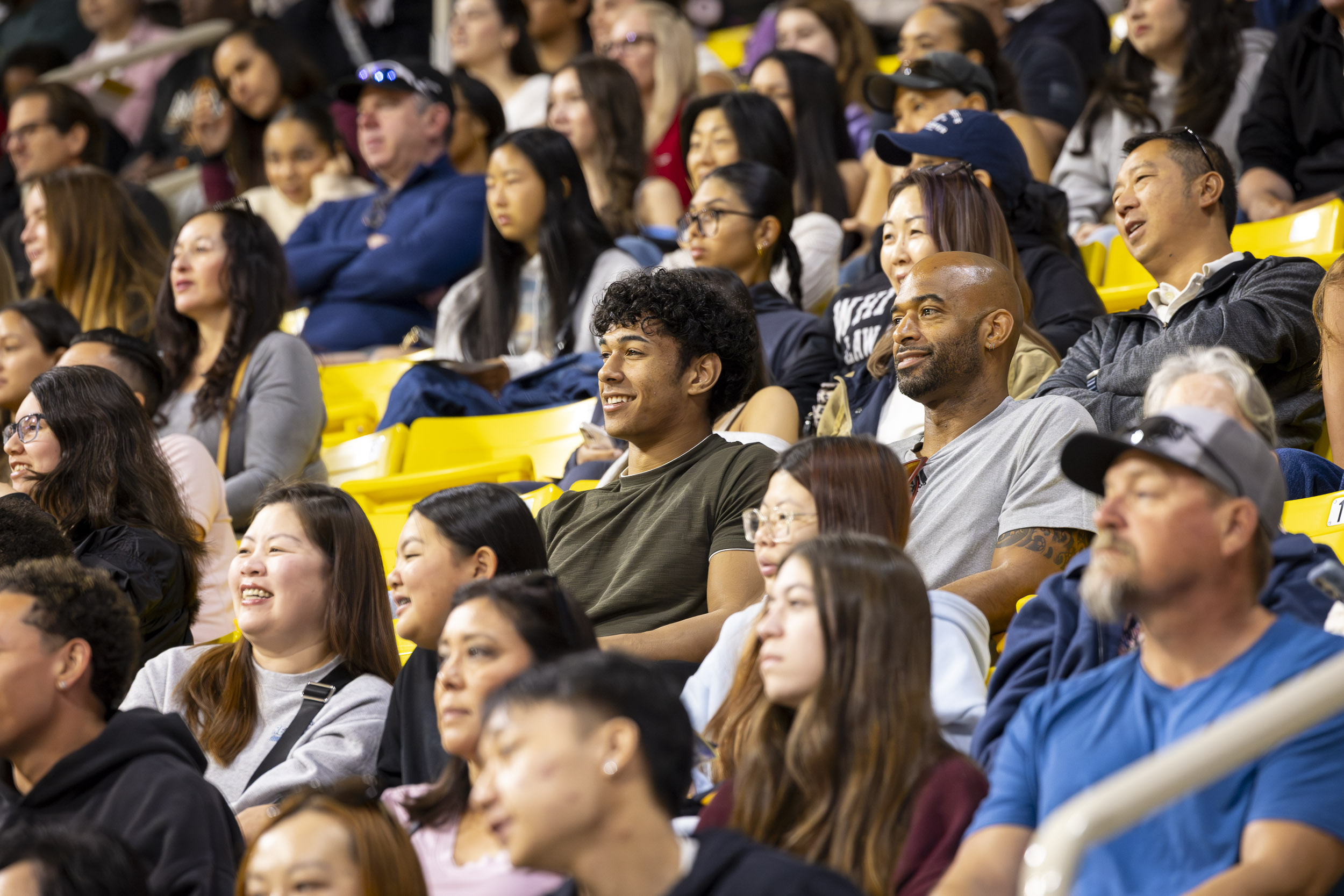 Audience of students and attendees sit closely together watching an event in arena seating.