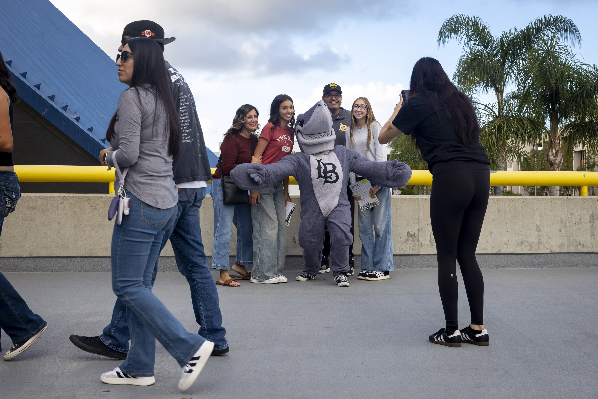 Group poses with campus mascot while another person takes their photo on outdoor walkway.