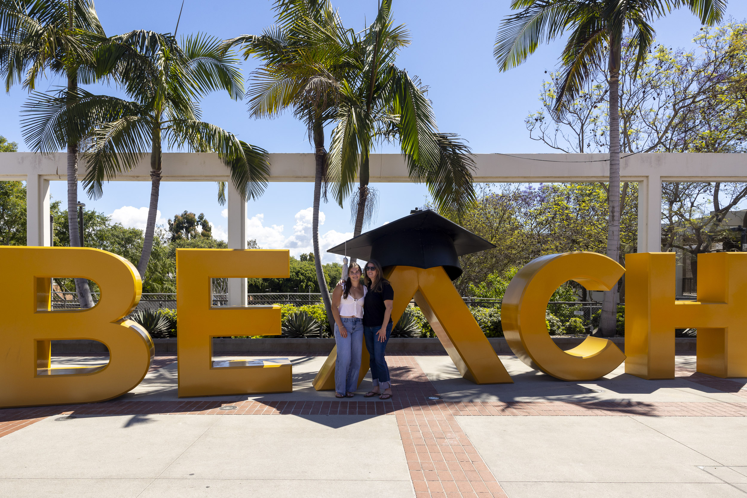 Two people stand in front of large BEACH letters posing for a photo on campus.