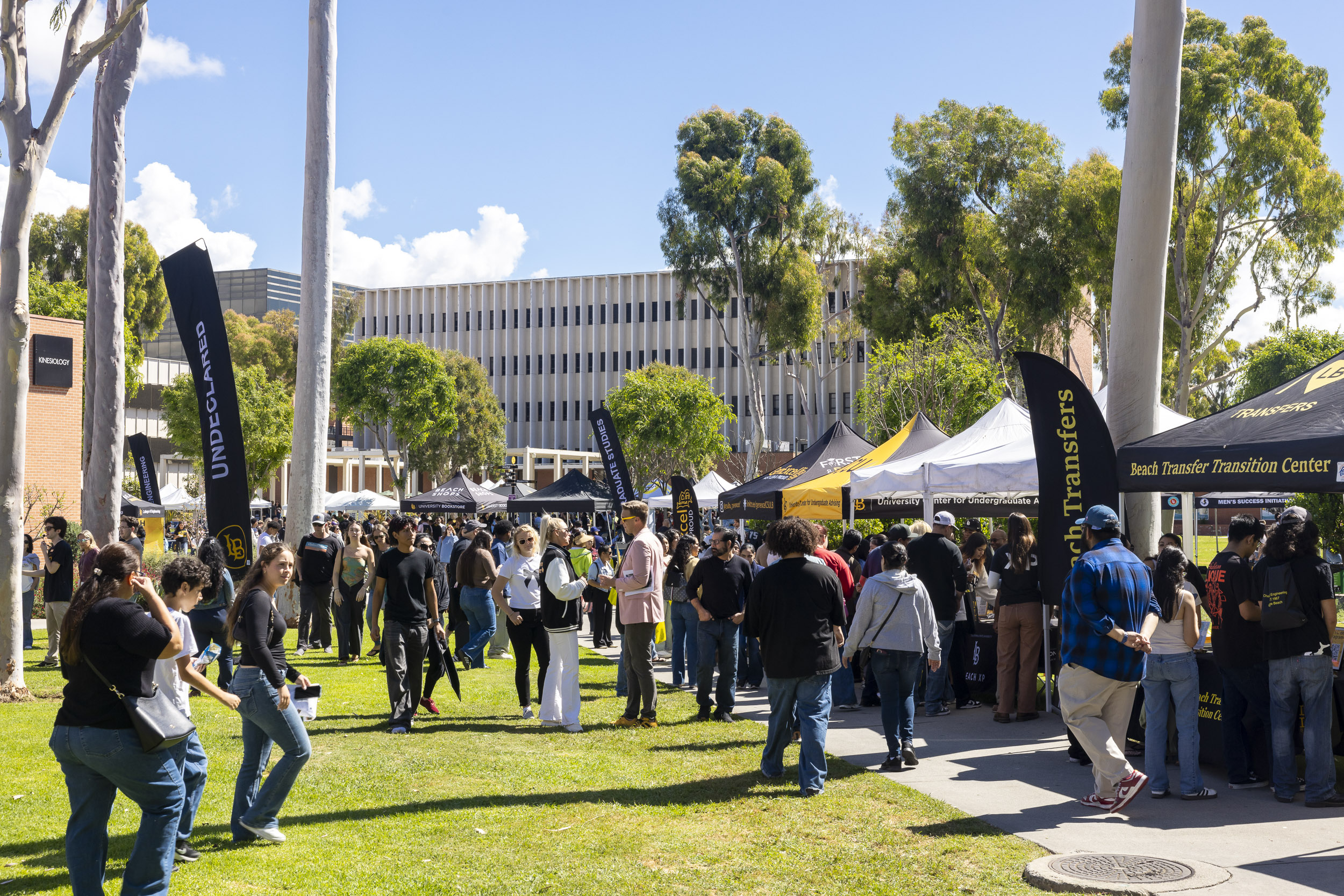 Crowd of students gathers around booths and tents at outdoor campus event.