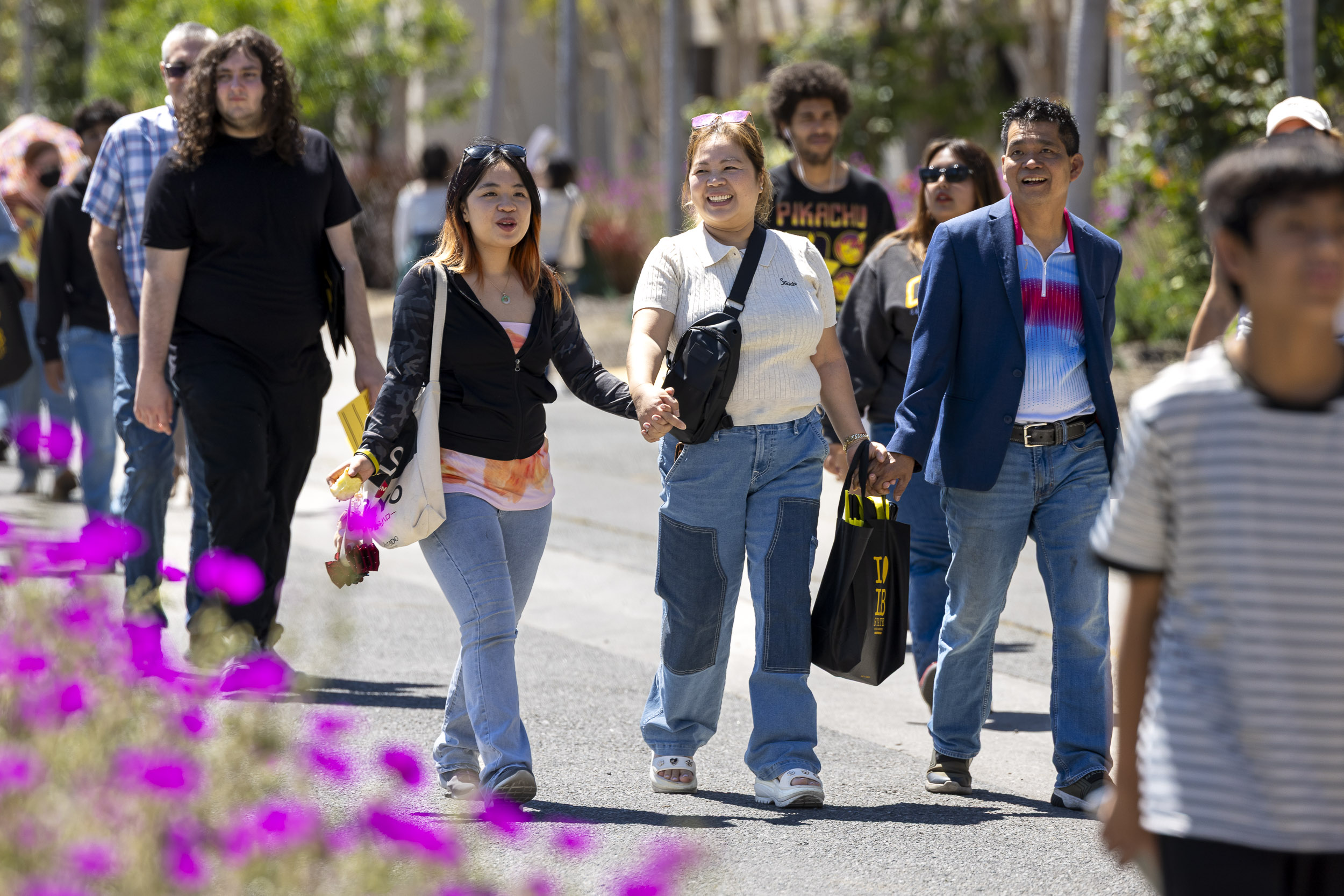 Group of people walk together along campus path smiling and holding hands