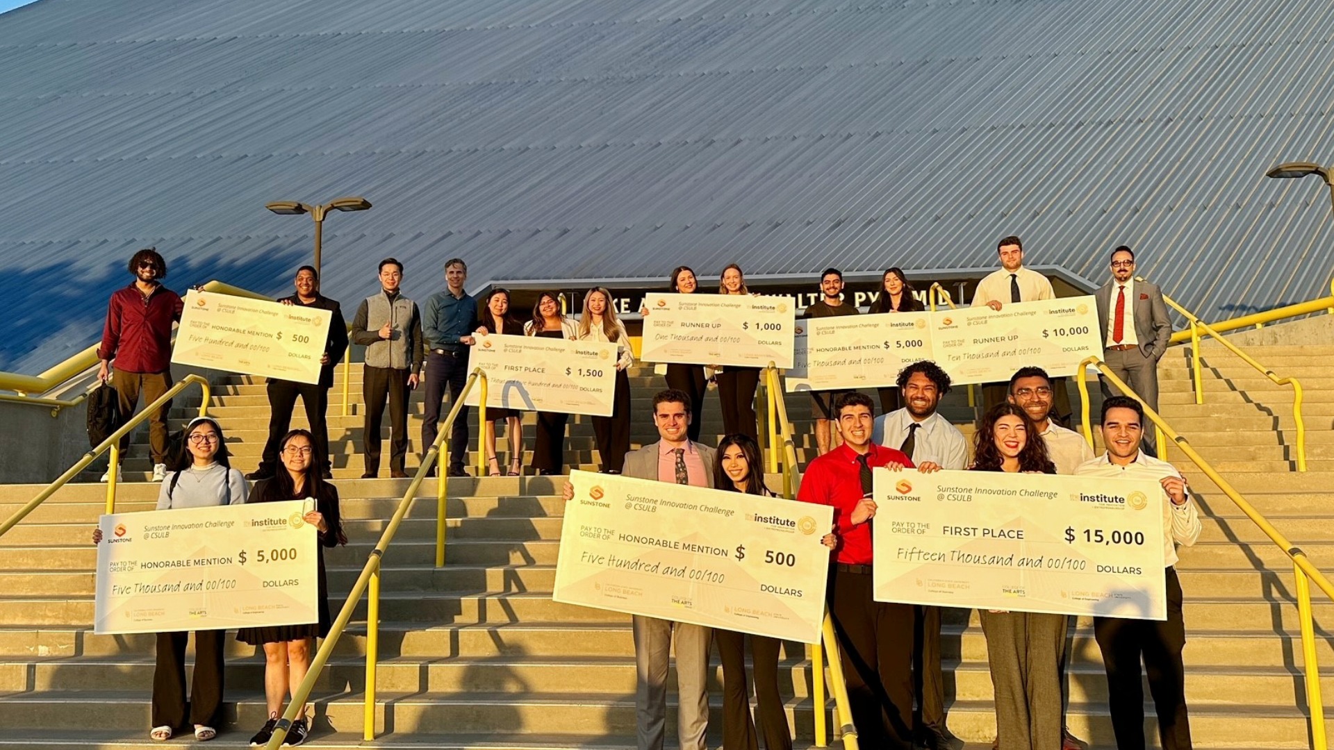 Students and faculty stand on campus steps holding oversized award checks after an innovation competition