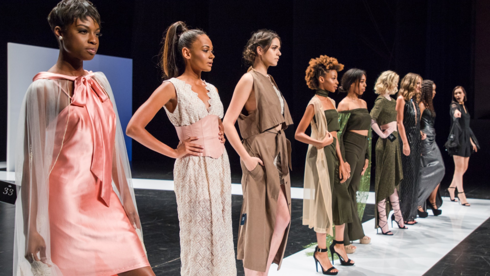 Models stand in a line on a runway during a fashion show.