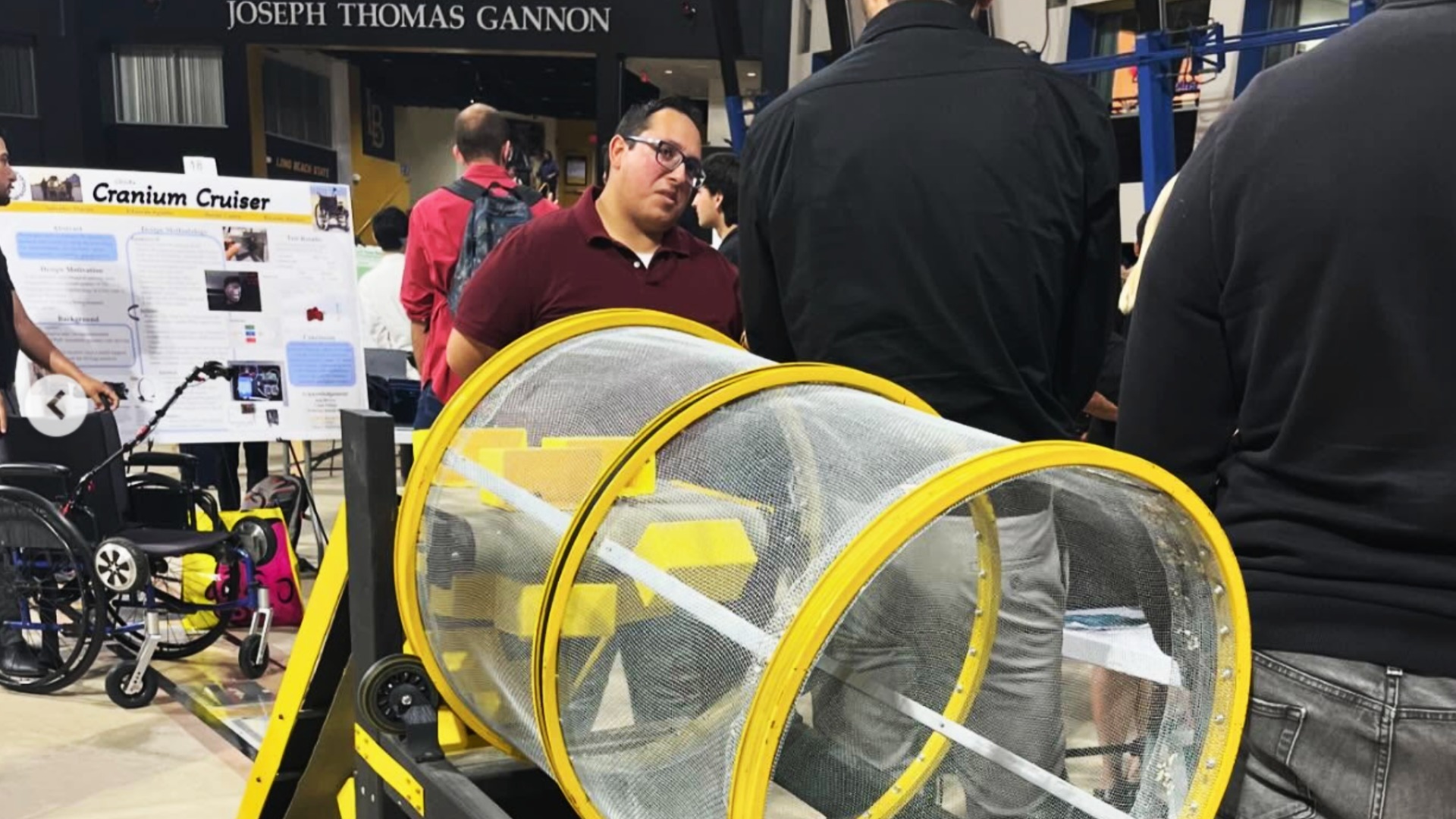 Students present an engineering project beside a large cylindrical device at a campus showcase.