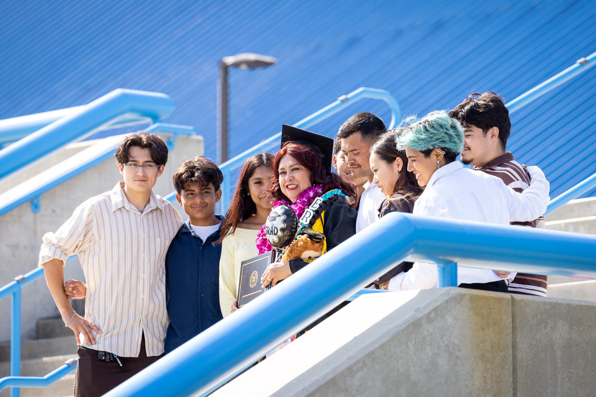A person in graduation regalia poses with a group on stadium steps