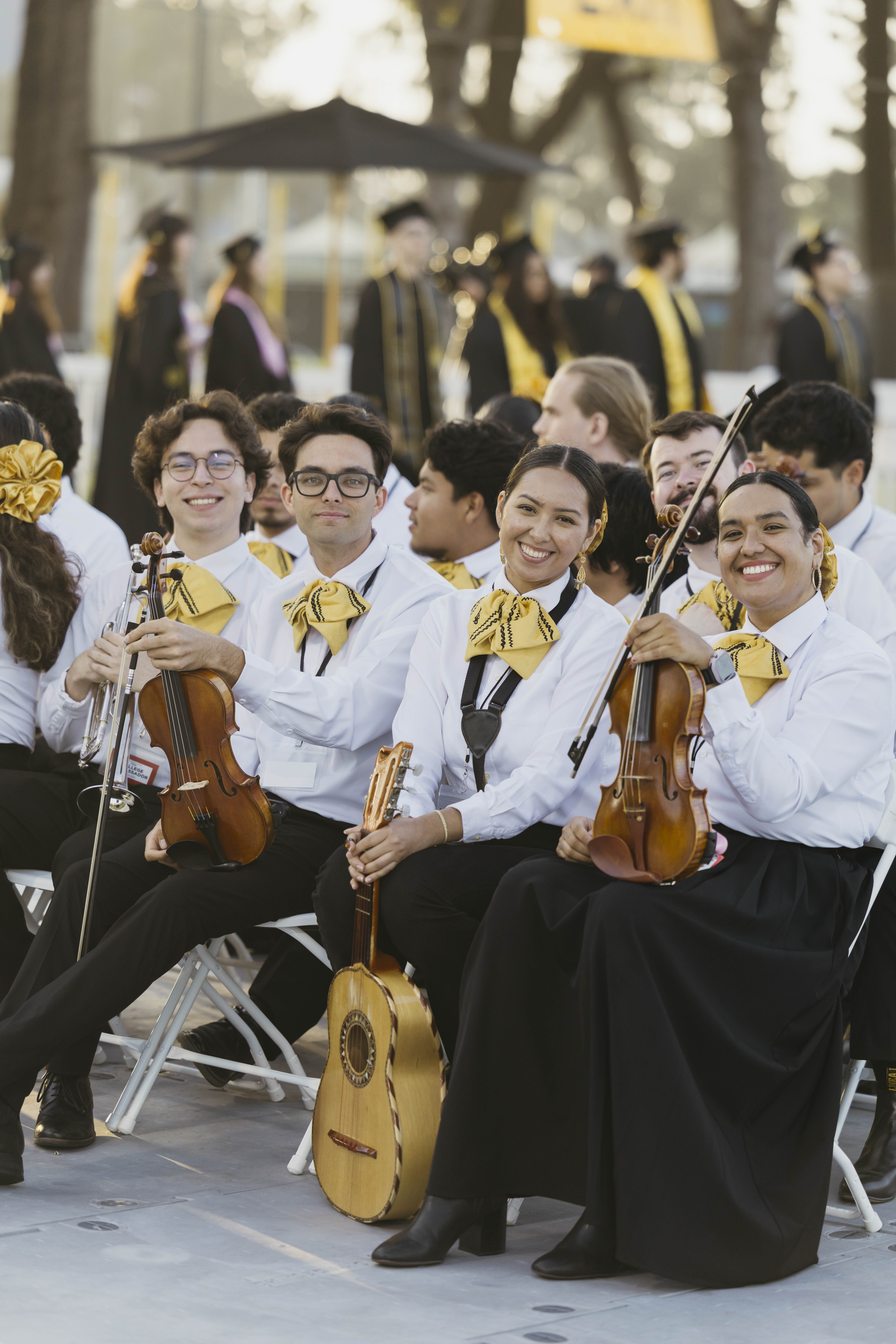 Mariachi musicians hold violins and smile at outdoor graduation ceremony