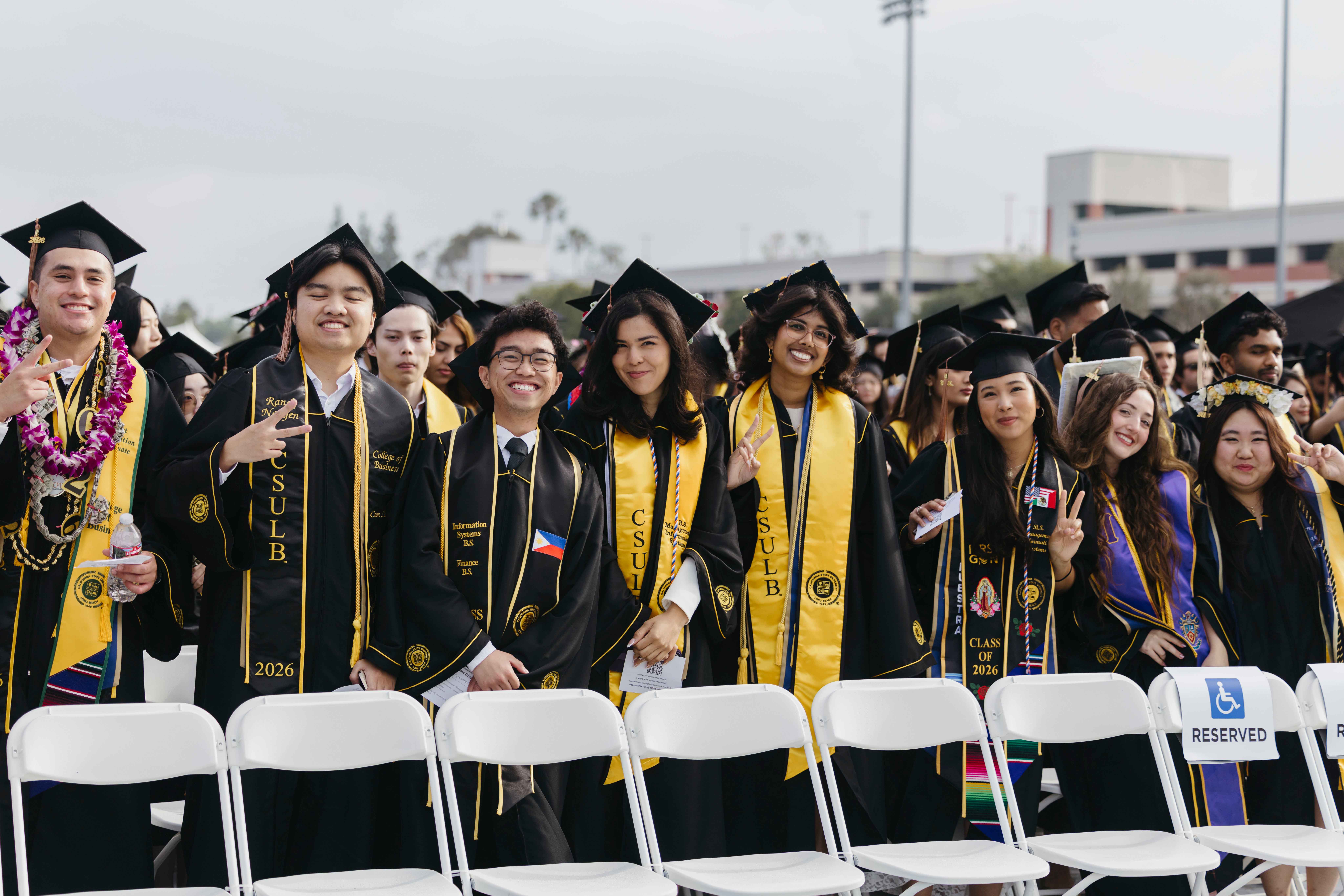 Group of graduates in caps and gowns smile and pose at outdoor ceremony