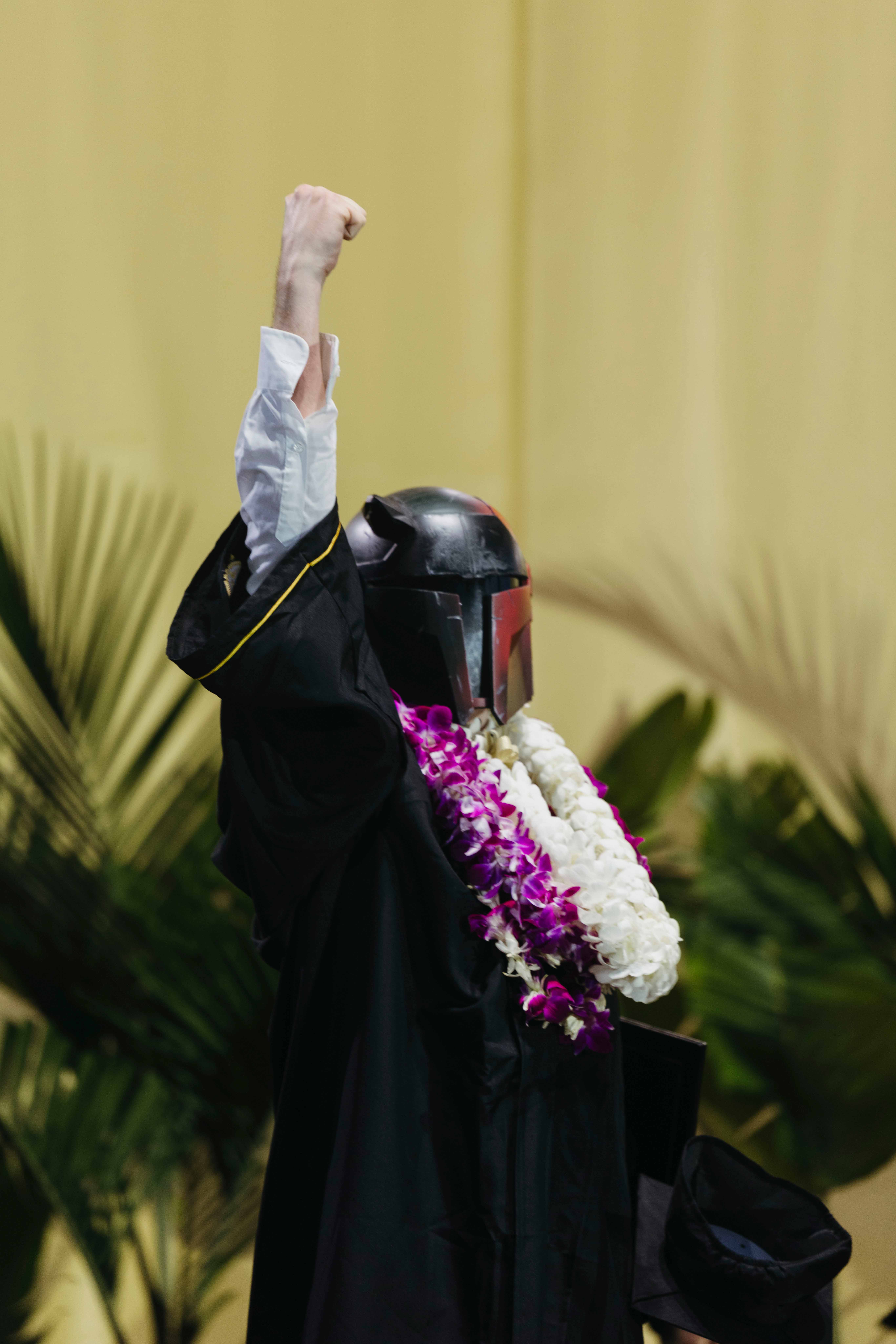 Graduate in cap and gown raises fist while wearing costume helmet