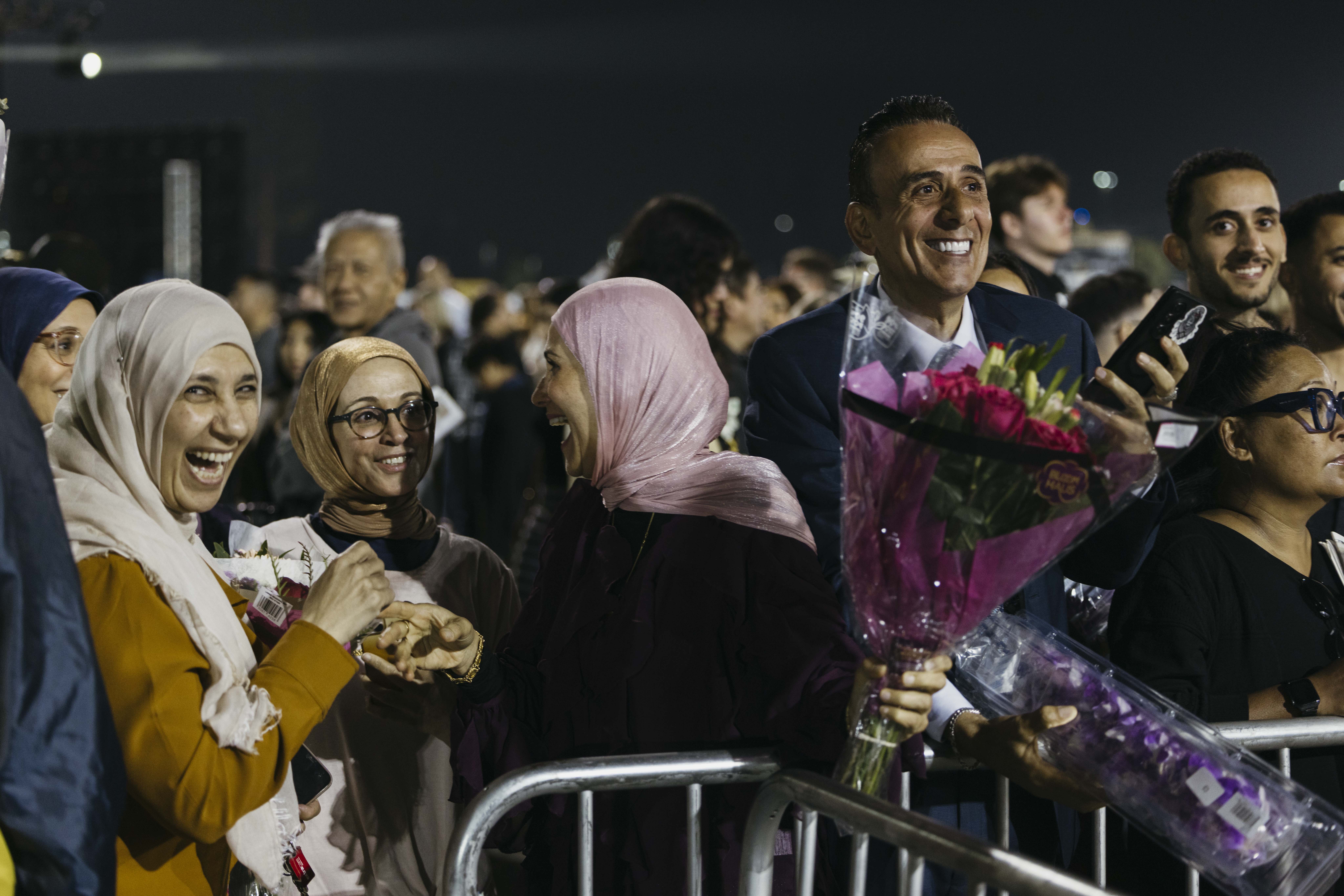 Group of people smile and hold flowers in crowd at nighttime ceremony