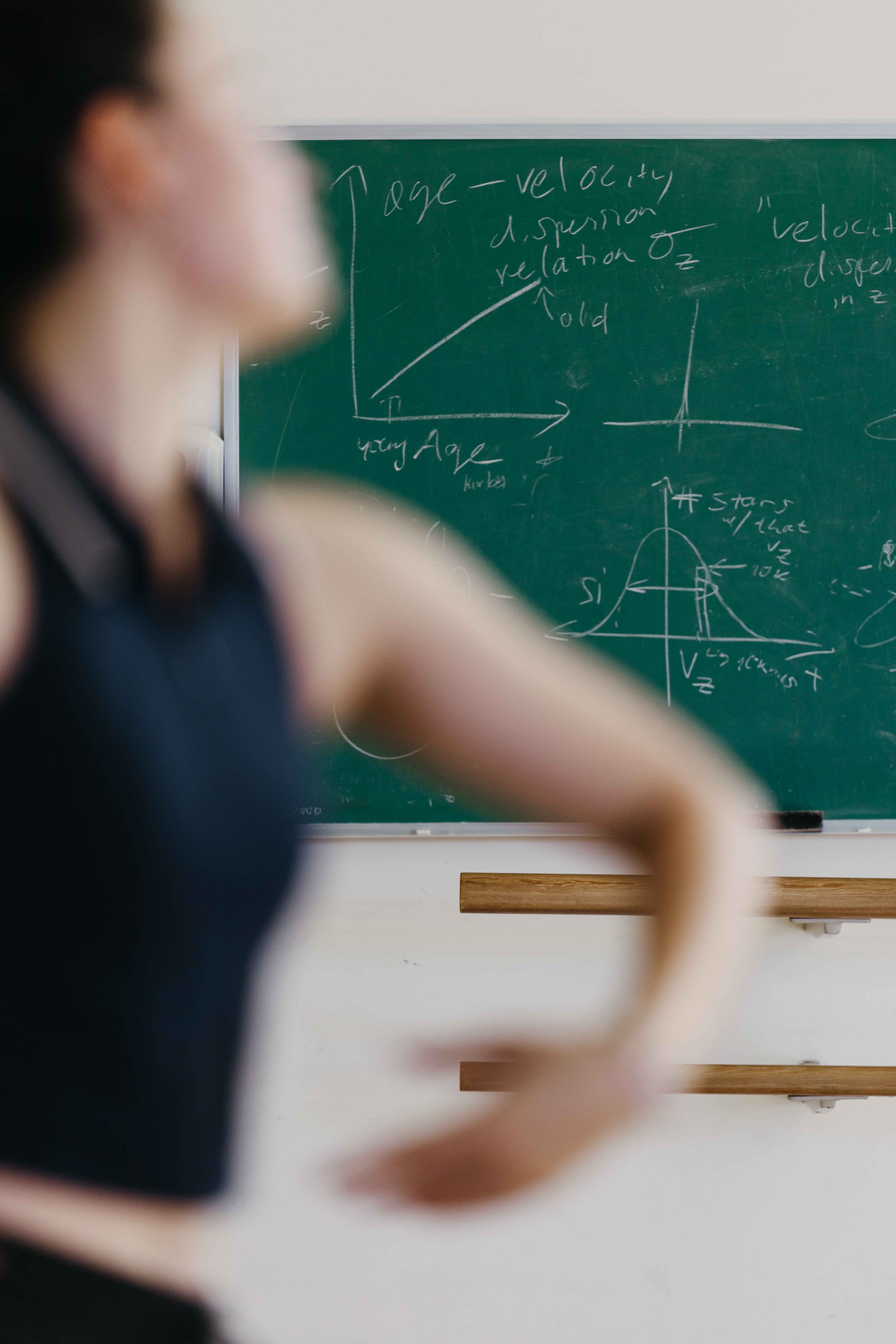 A person moves in front of a chalkboard covered in physics diagrams and equations