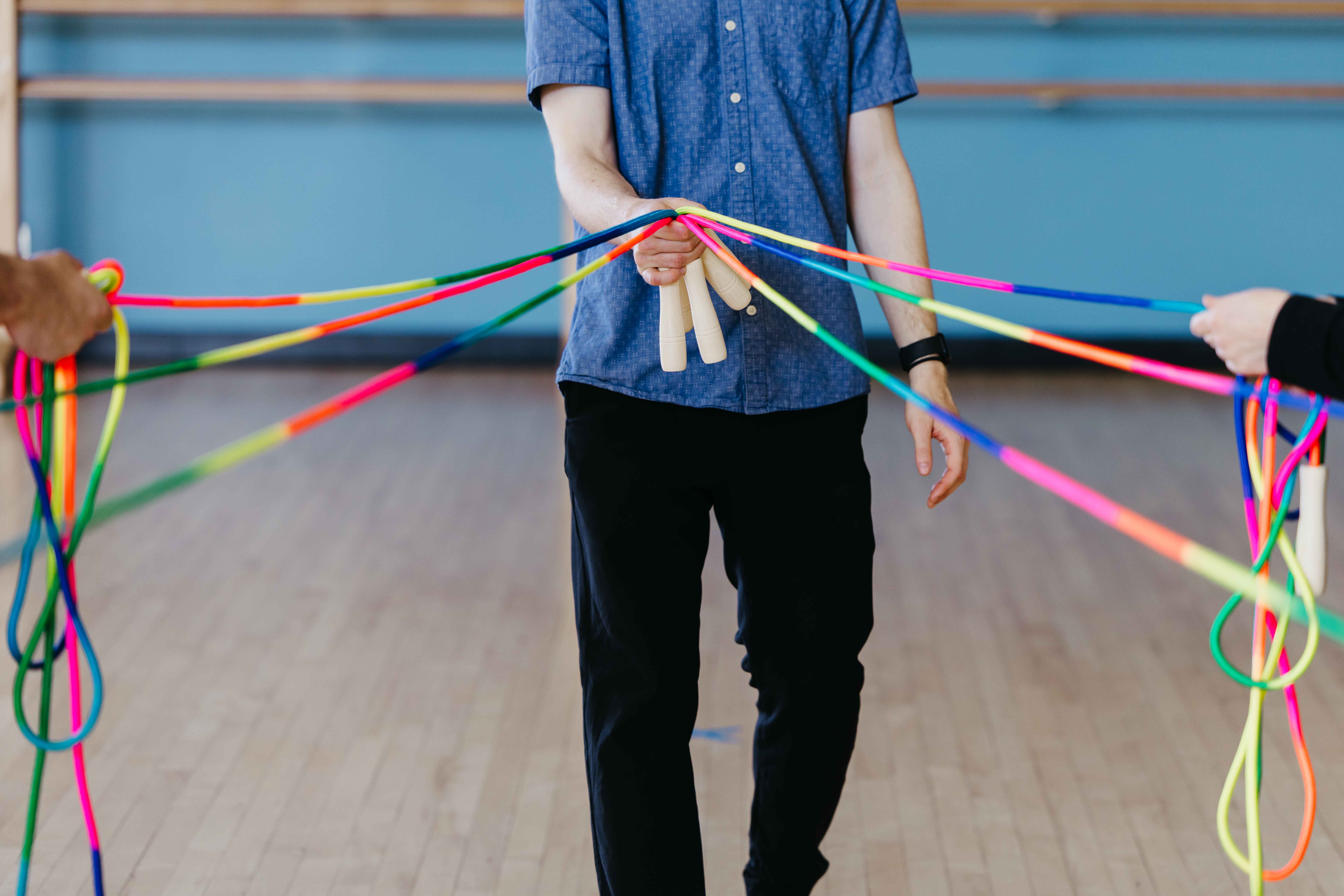 A person holds multiple colorful jump ropes extending outward in a dance studio