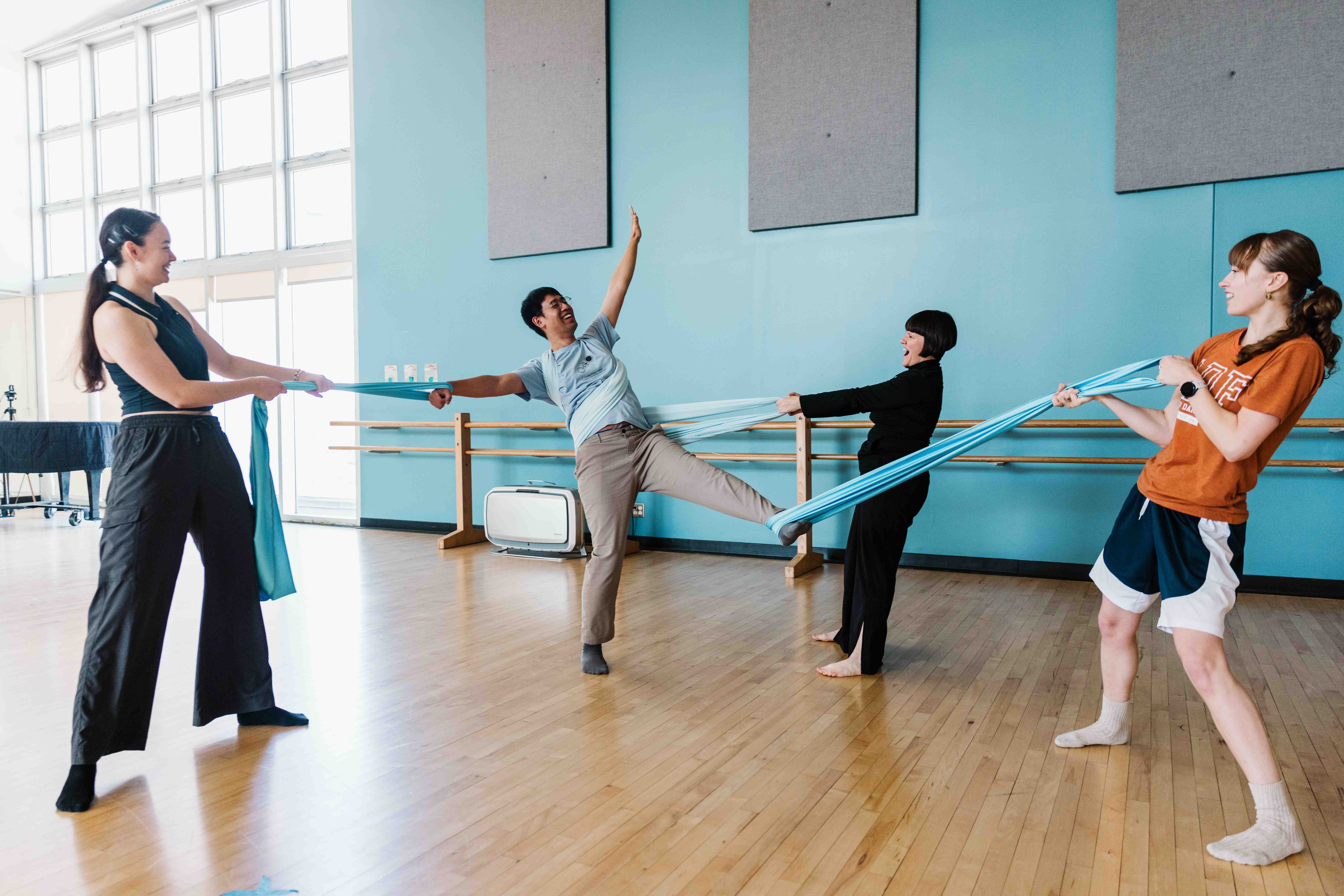 Four people stretch a blue fabric between them in a dance studio