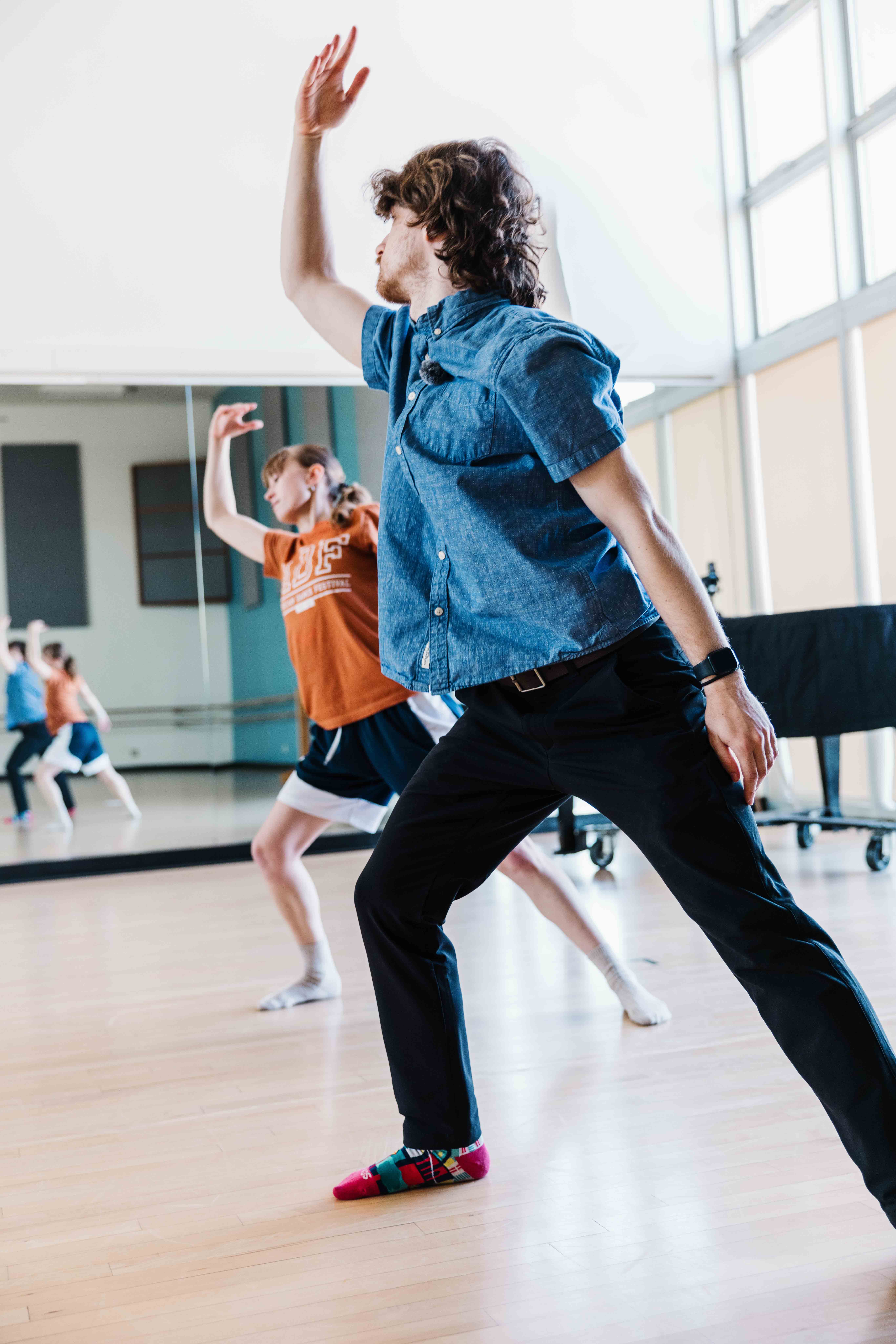 A person dances with one arm raised in a mirrored studio