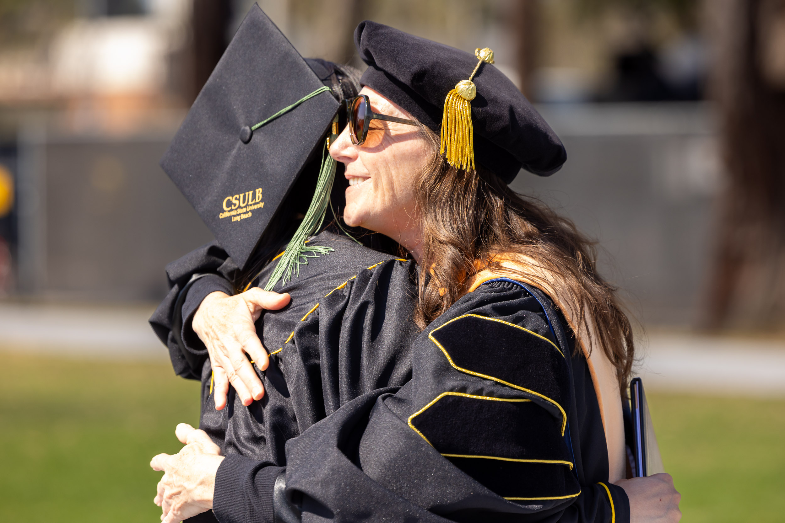 Two people in commencement regalia embrace 