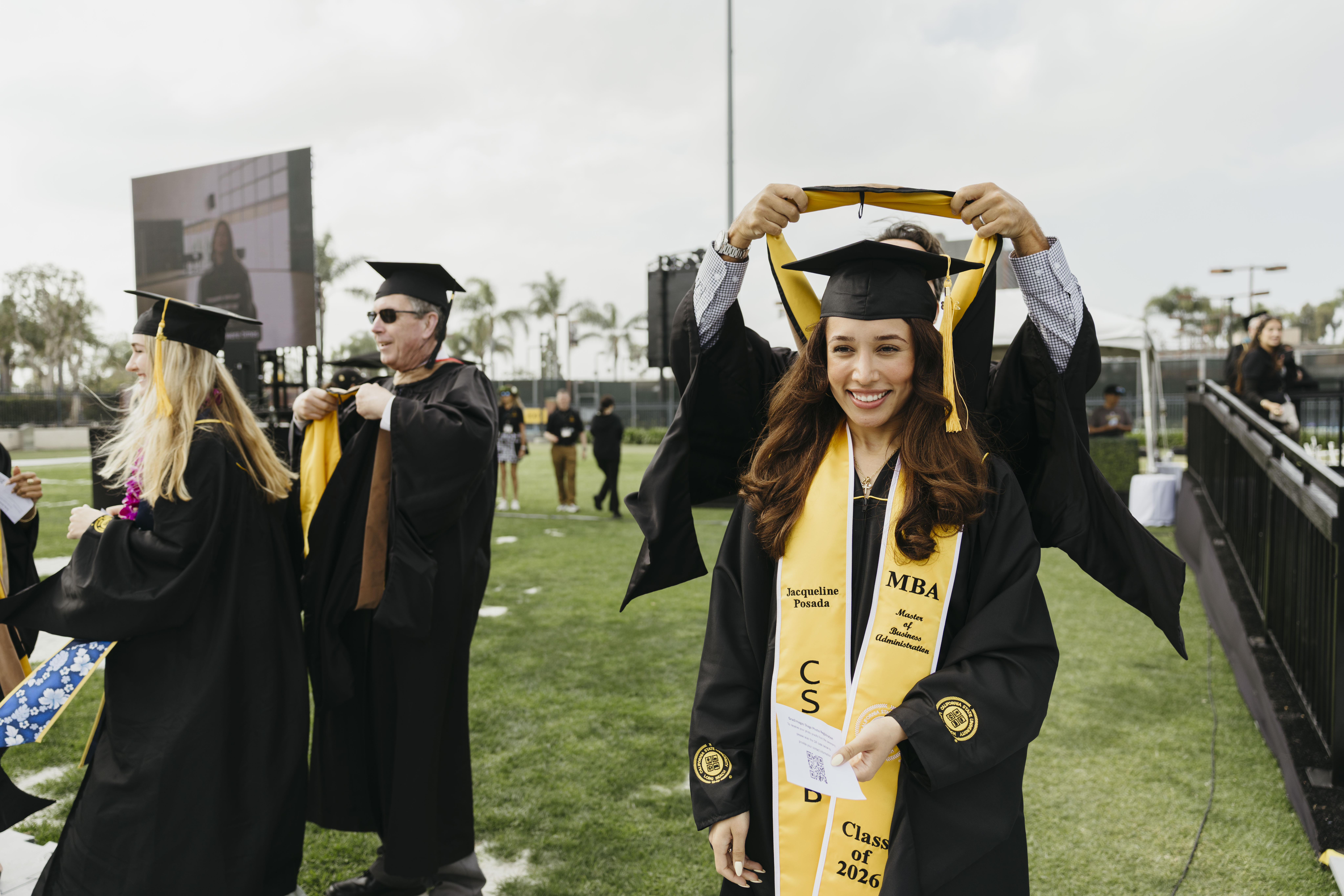 Graduate receives master's stole while smiling at outdoor commencement ceremony