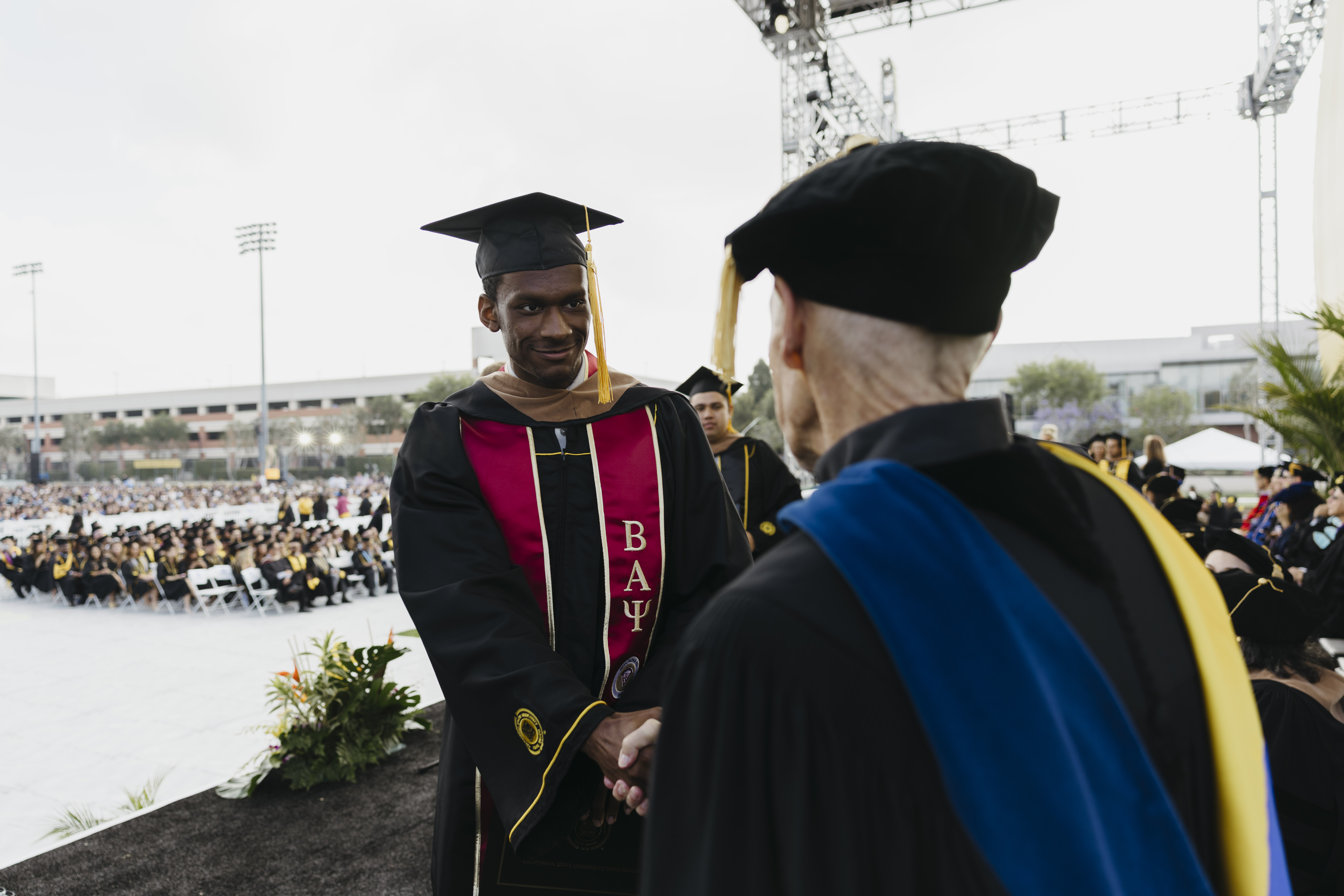 Graduate shakes hands with faculty member on stage at outdoor ceremony
