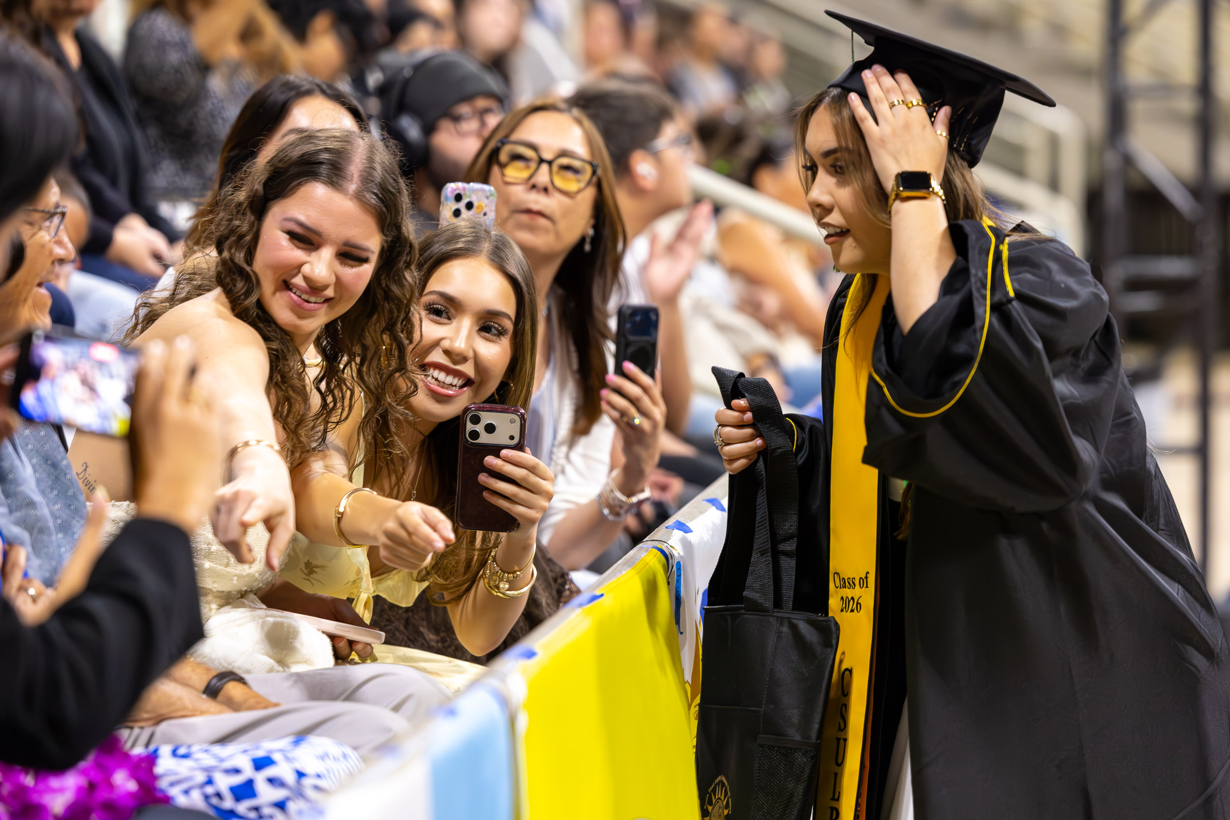 Graduate greets family members taking photos in arena stands