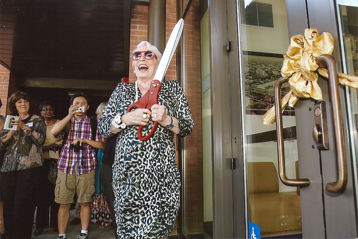 Regena Cole laughing while holding a pair of ceremonial scissors for the ribbon cutting at a door