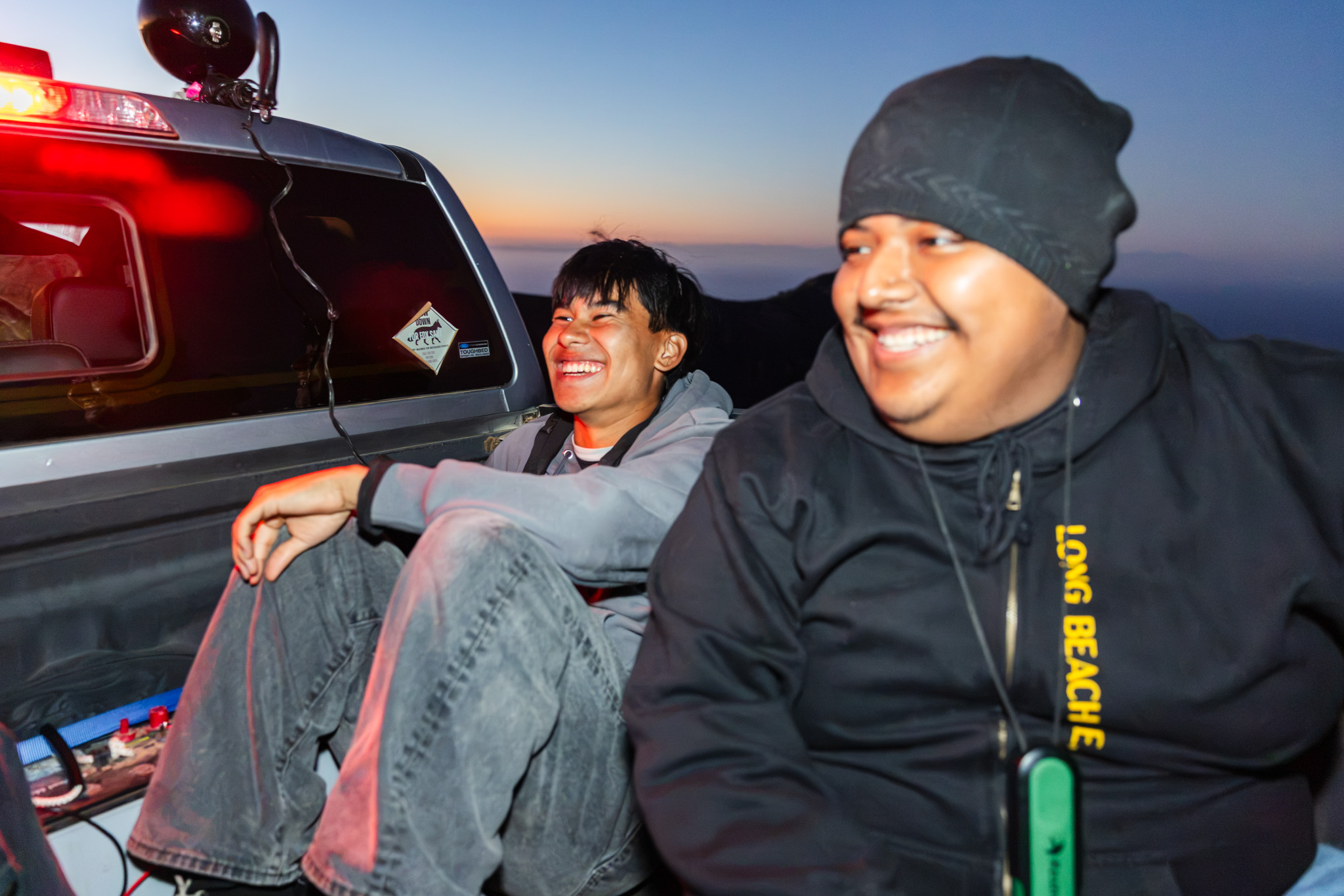 Two people sit in a truck bed laughing together at dusk