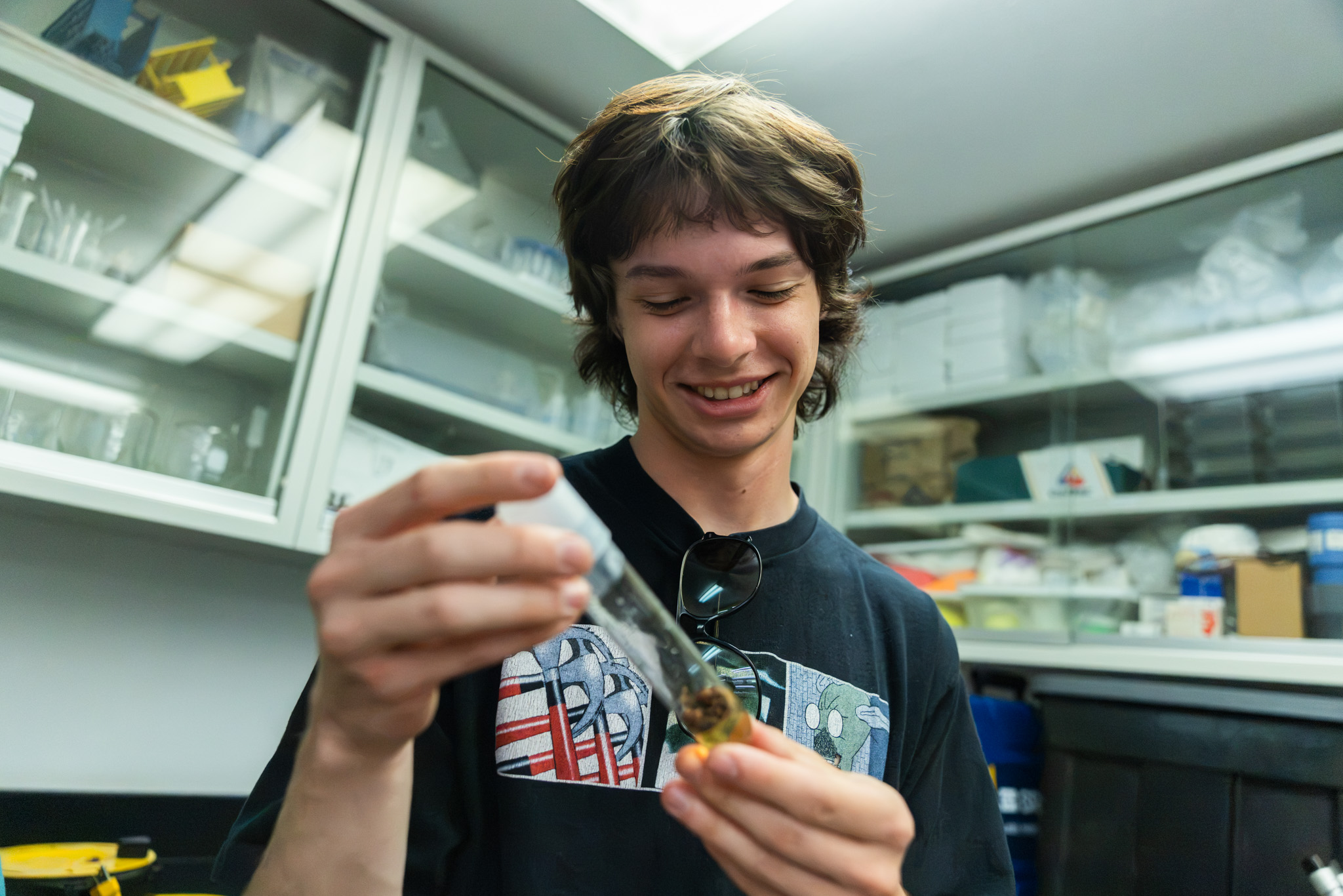 A person smiles while holding a vial in a lab setting