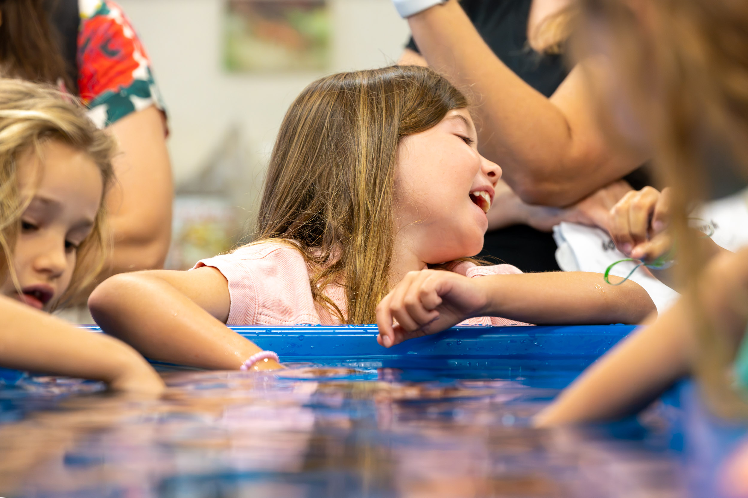A child laughs while leaning over the edge of a touch tank