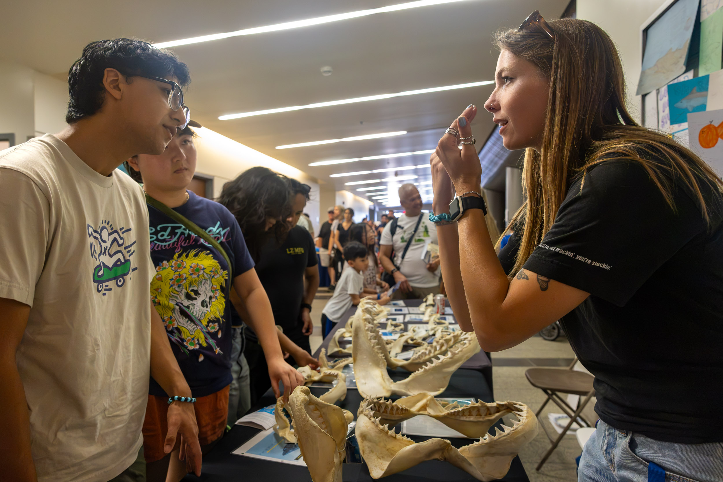 A person gestures while talking with two attendees at a shark jaw display