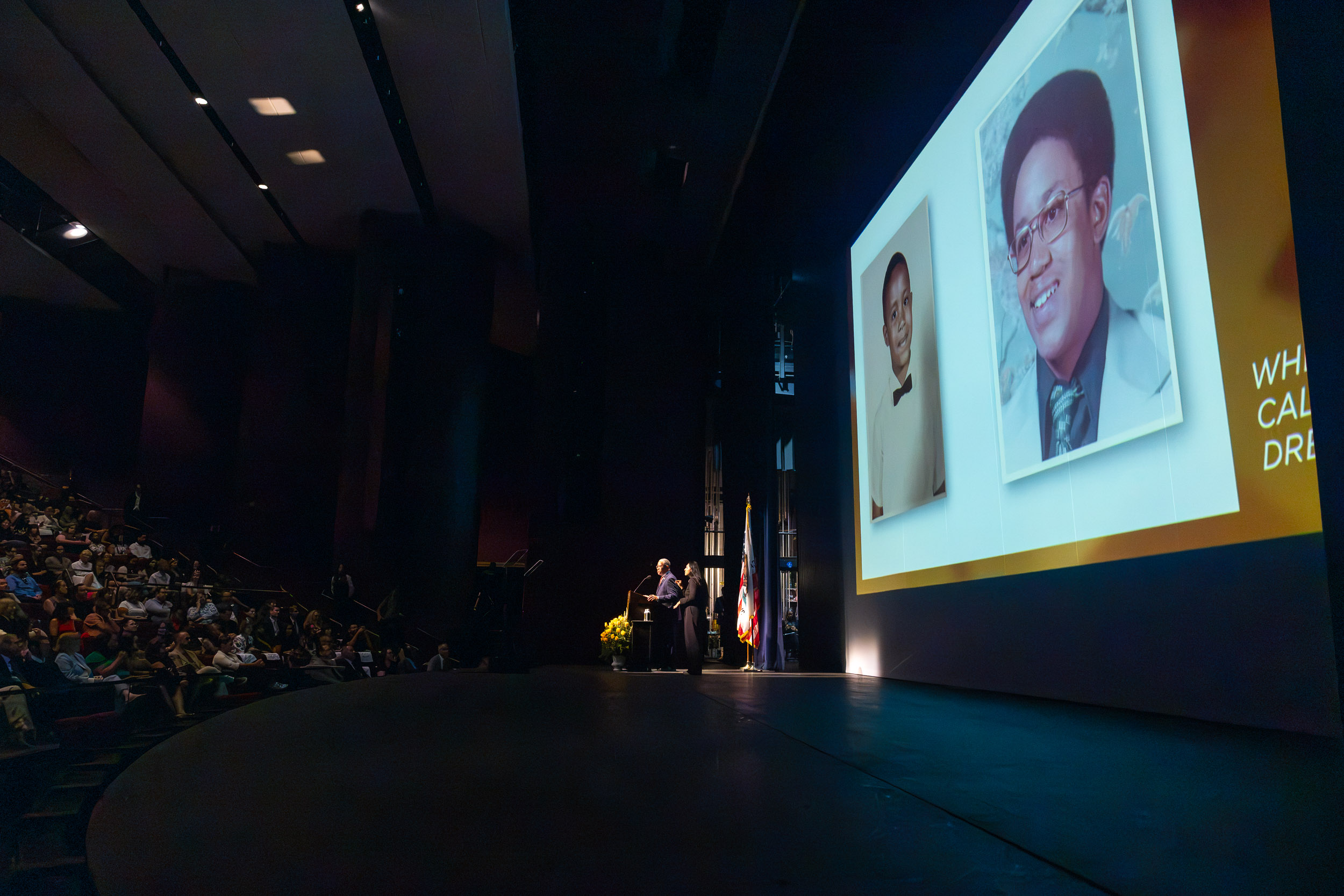 President Loren J. Blanchard speaking, with a projection of photos of when he was younger