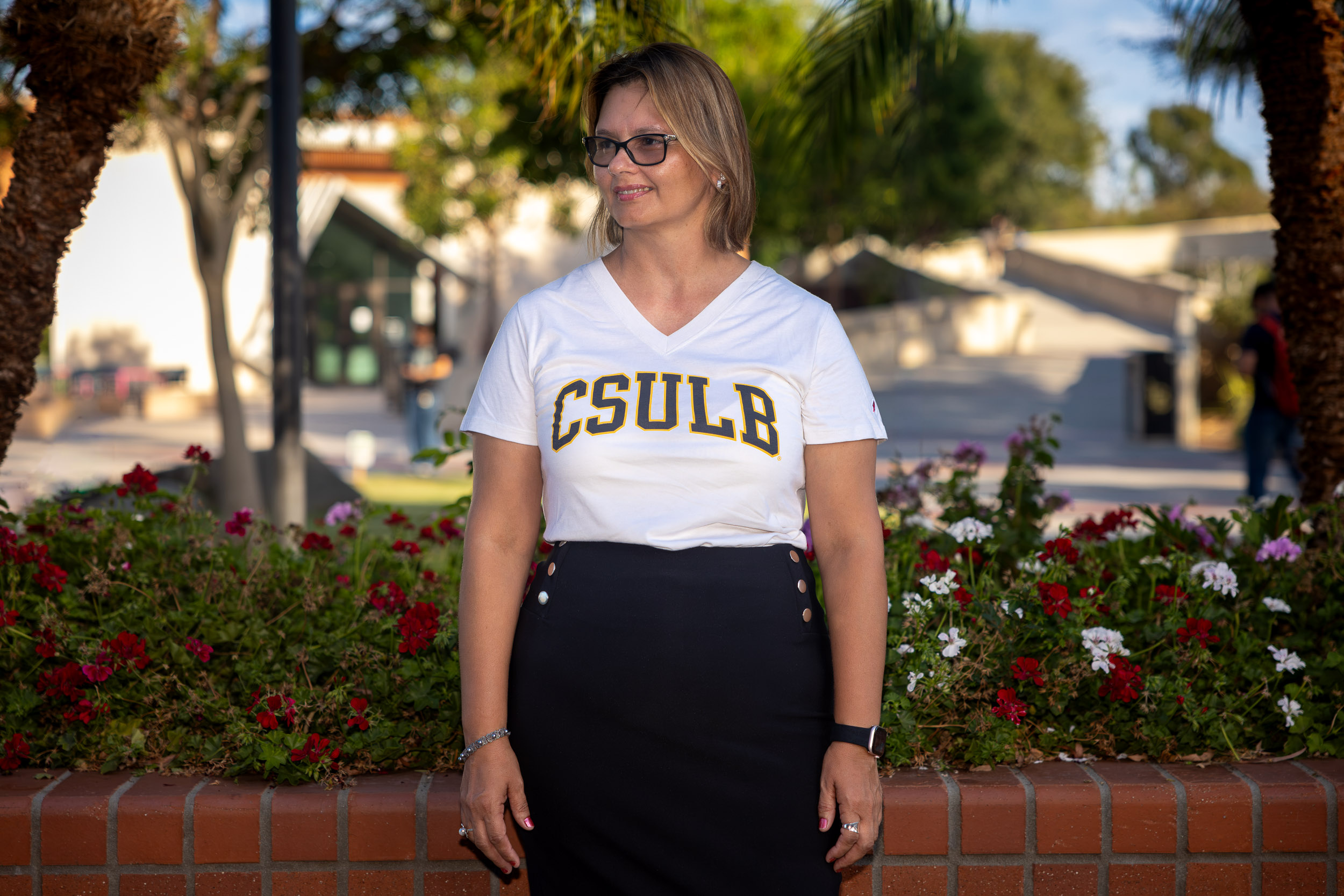 A person stands in front of a brick wall wearing a CSULB T-shirt.