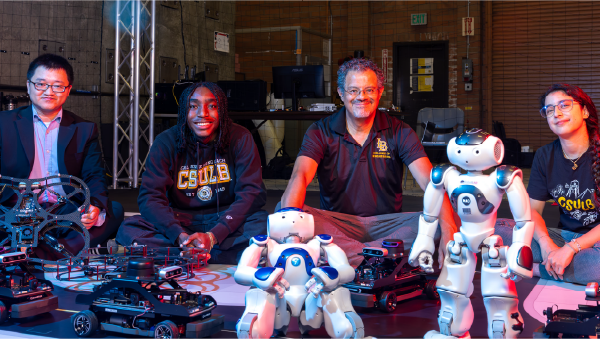 Four people pose with robots and small autonomous vehicles during a robotics demonstration.
