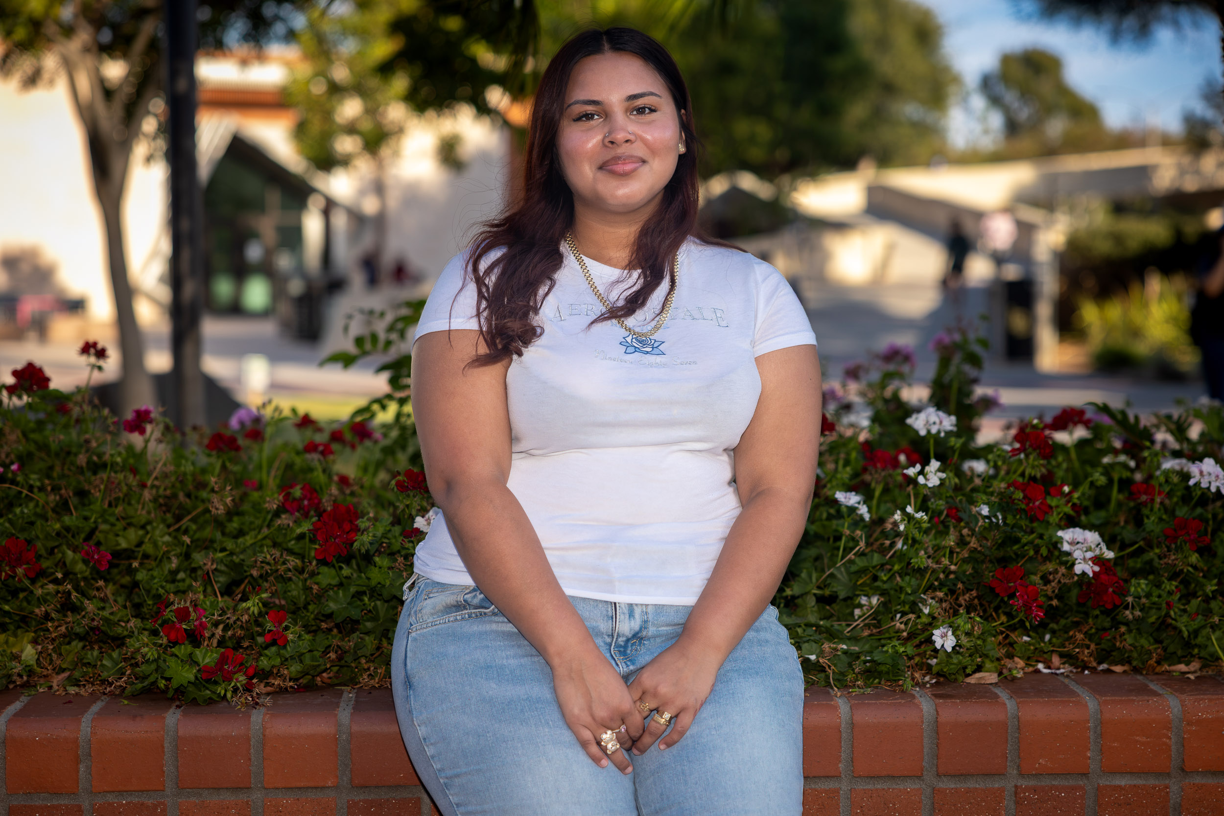A person sits on a low brick wall smiling
