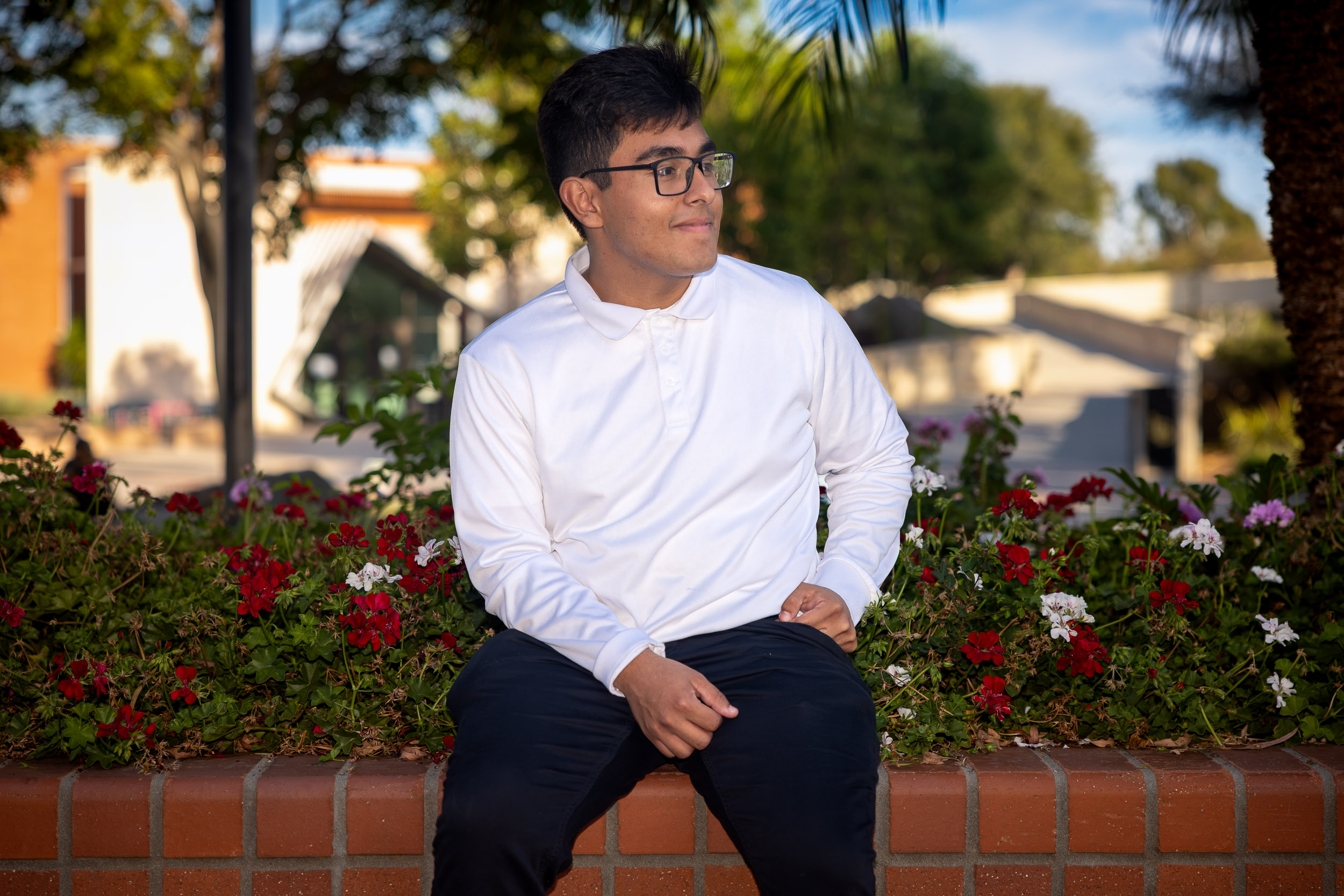 A person in glasses sits on a low brick walk looking into the distance