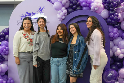 Attendees taking a group photo in front of a purple balloon arch.