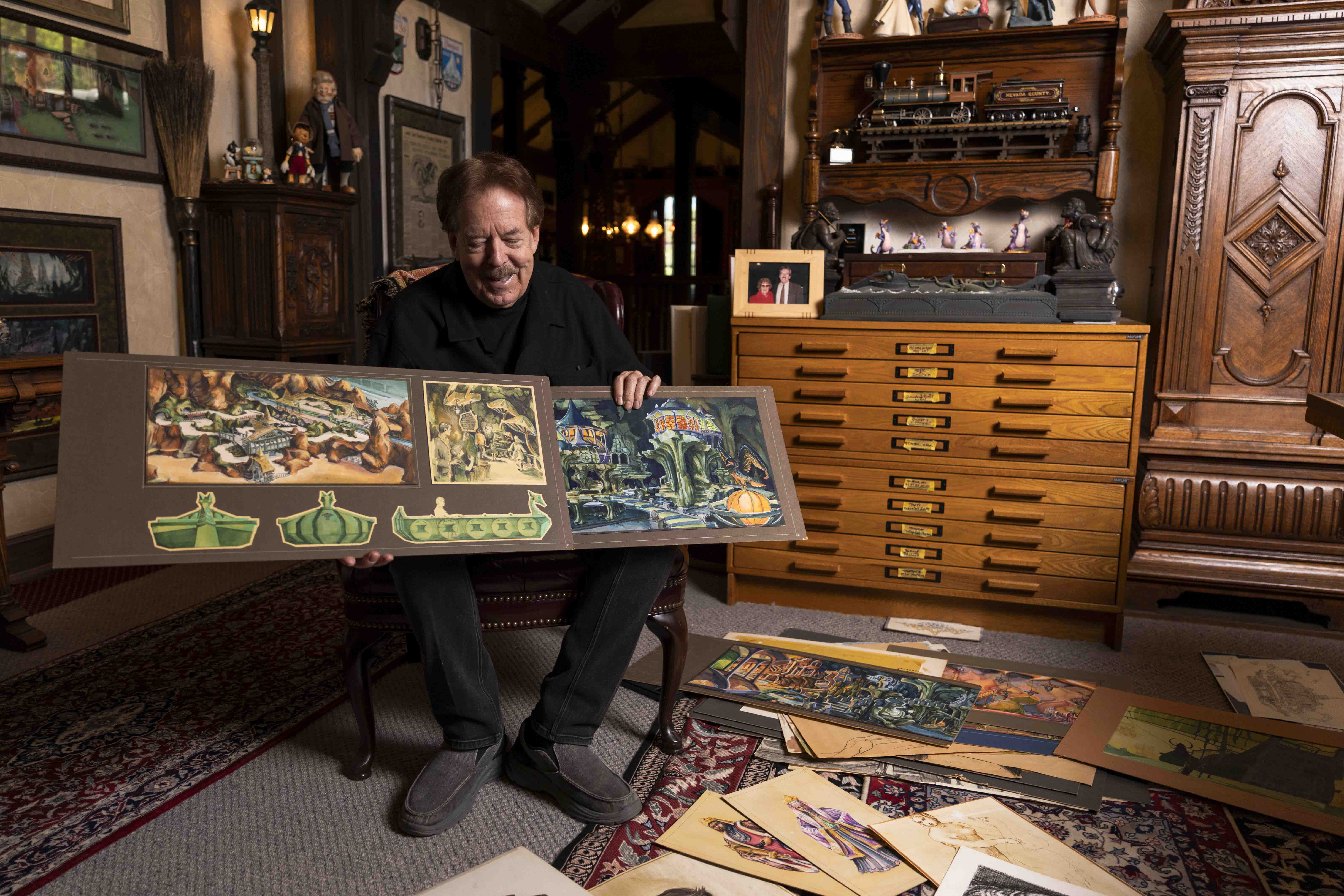 A person sits in a room holding two renderings attached to a board