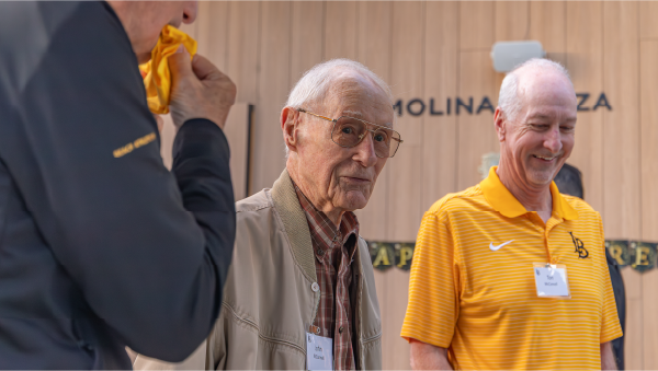 Two alumni stand together at an indoor university event.