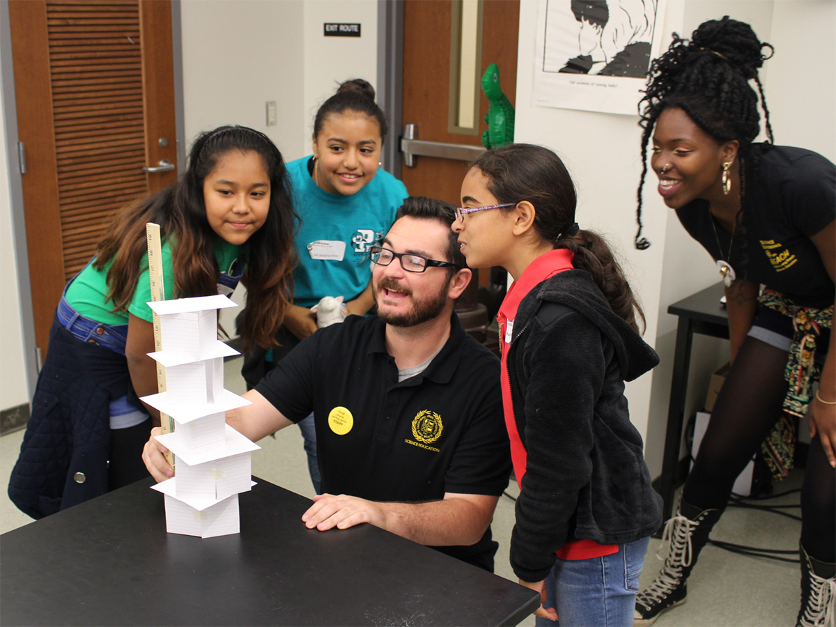 teacher measuring index card tower as young learners watch with excitement