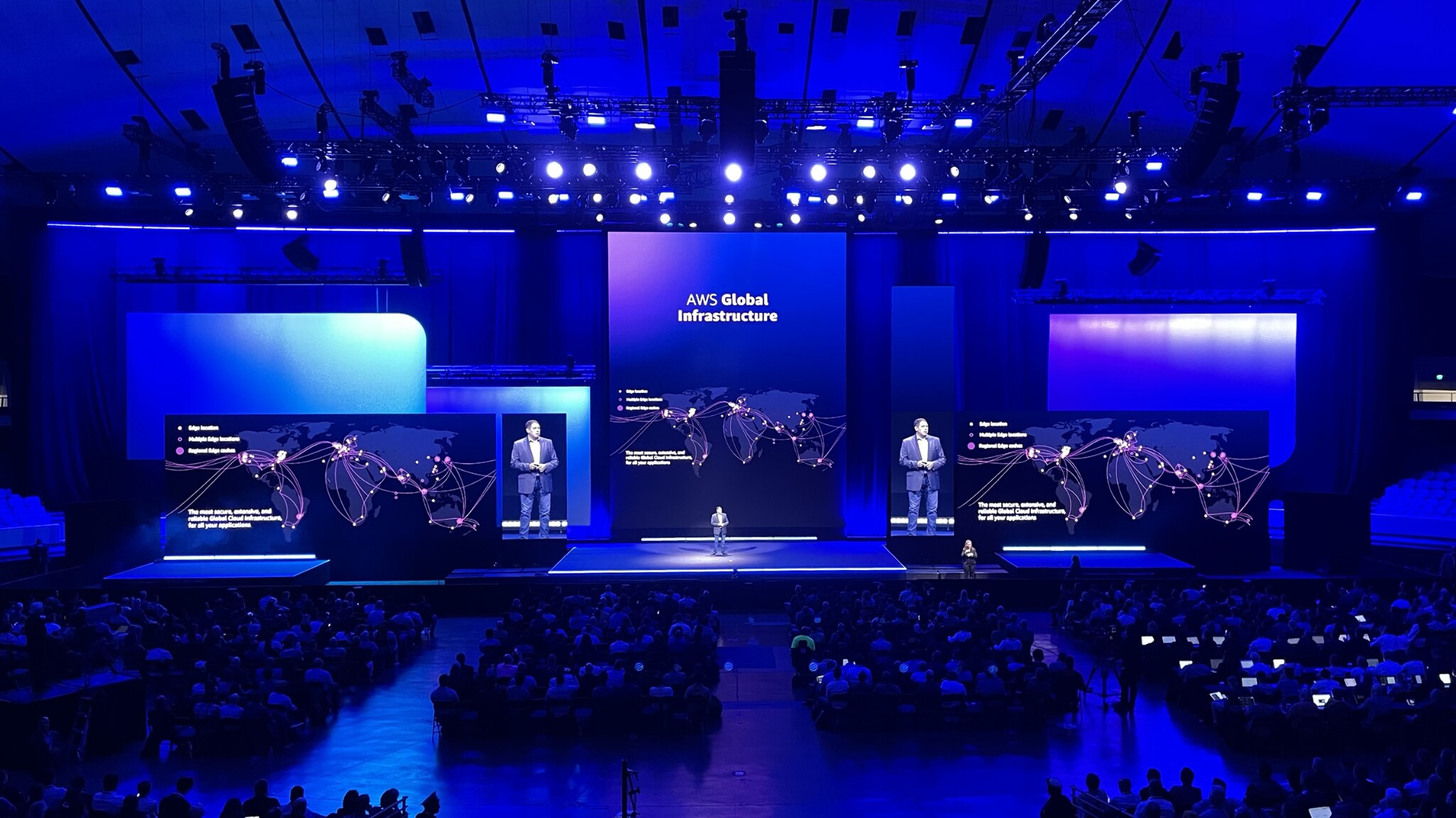 AWS conference presentation about global infrastructure displayed across a large, blue-lit stage. Created by Taylor Gibbs