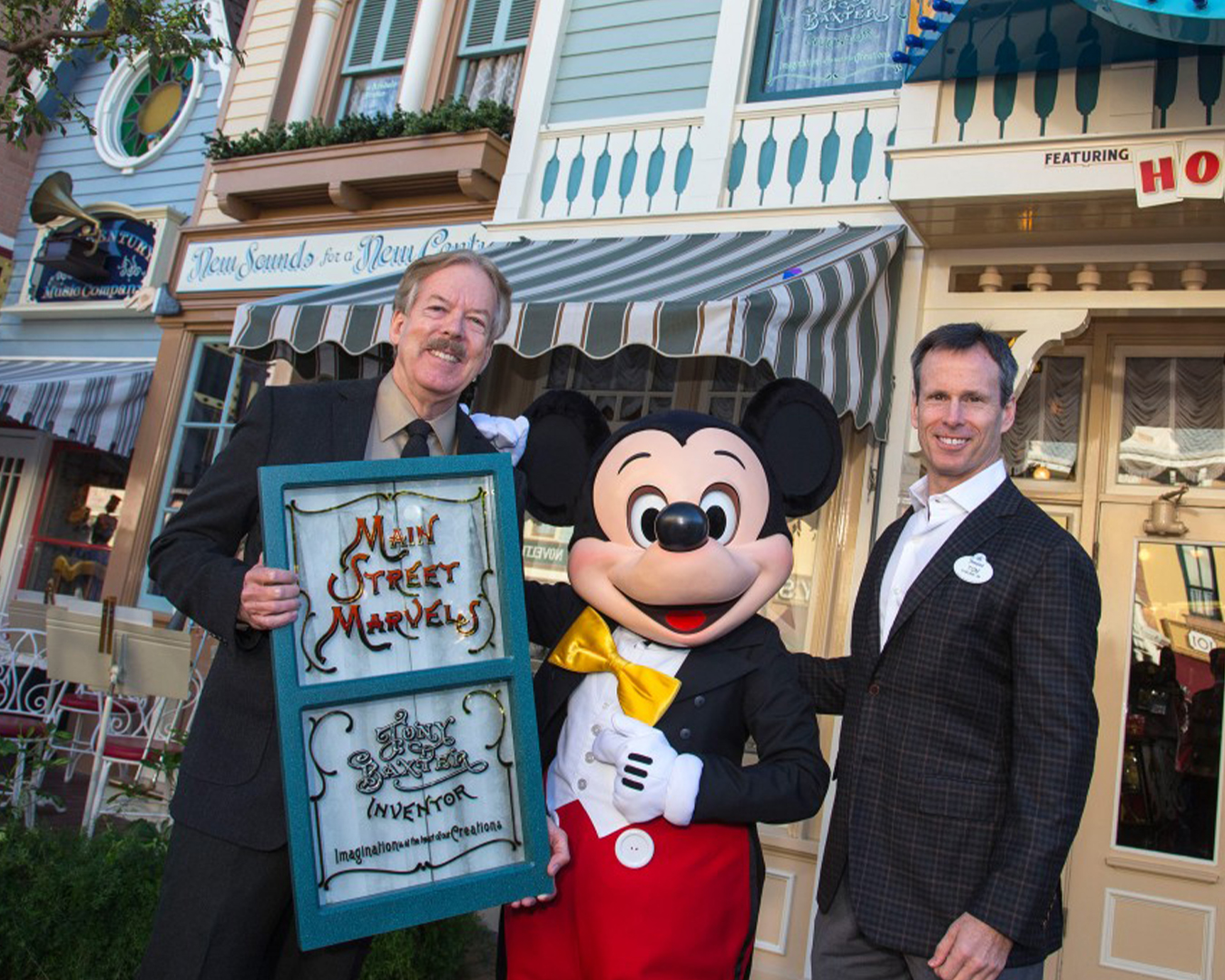 A person in a Mickey Mouse costume is flanked by two men