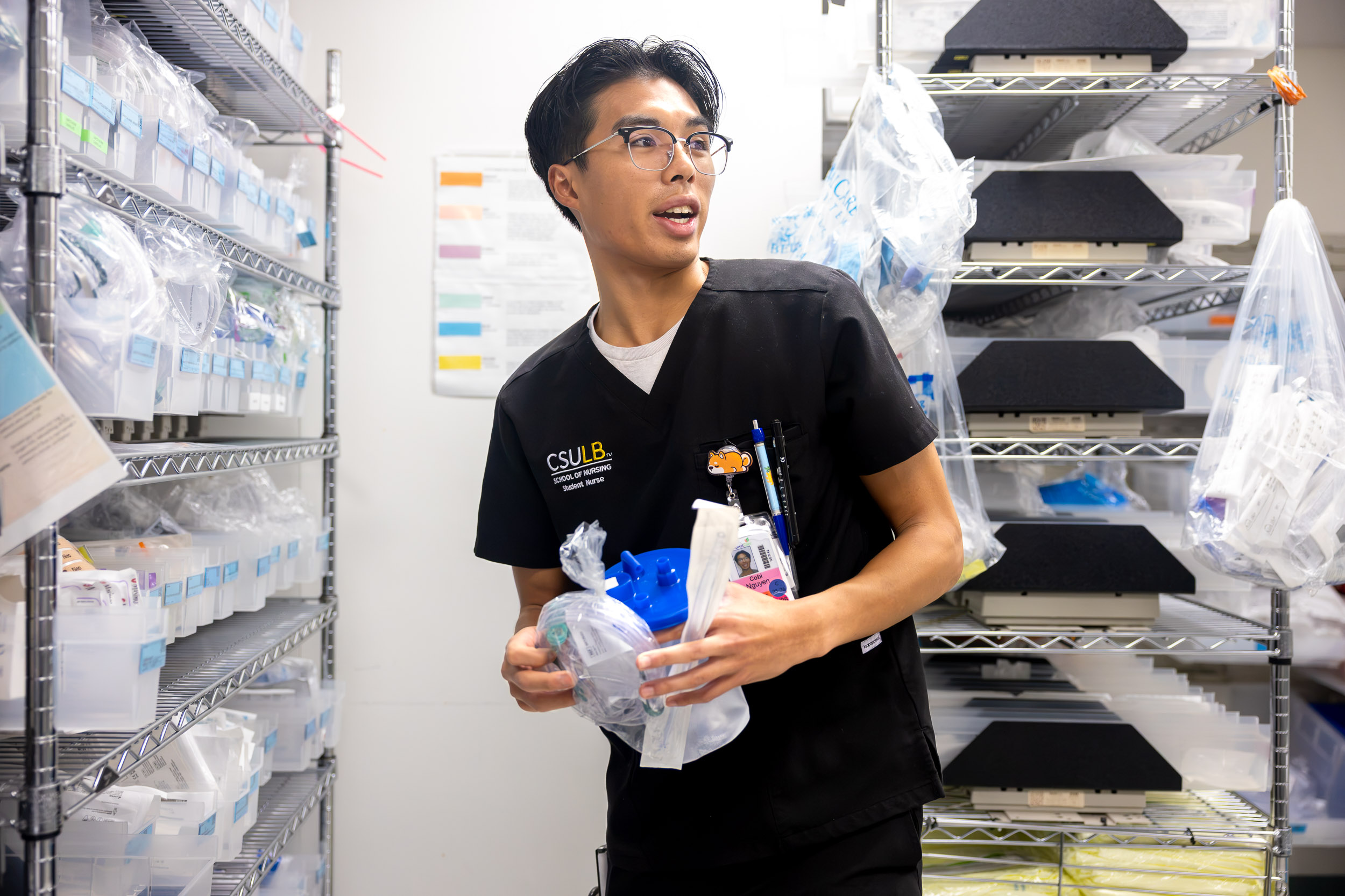 A person in scrubs carries medical supplies in a hospital supply room.