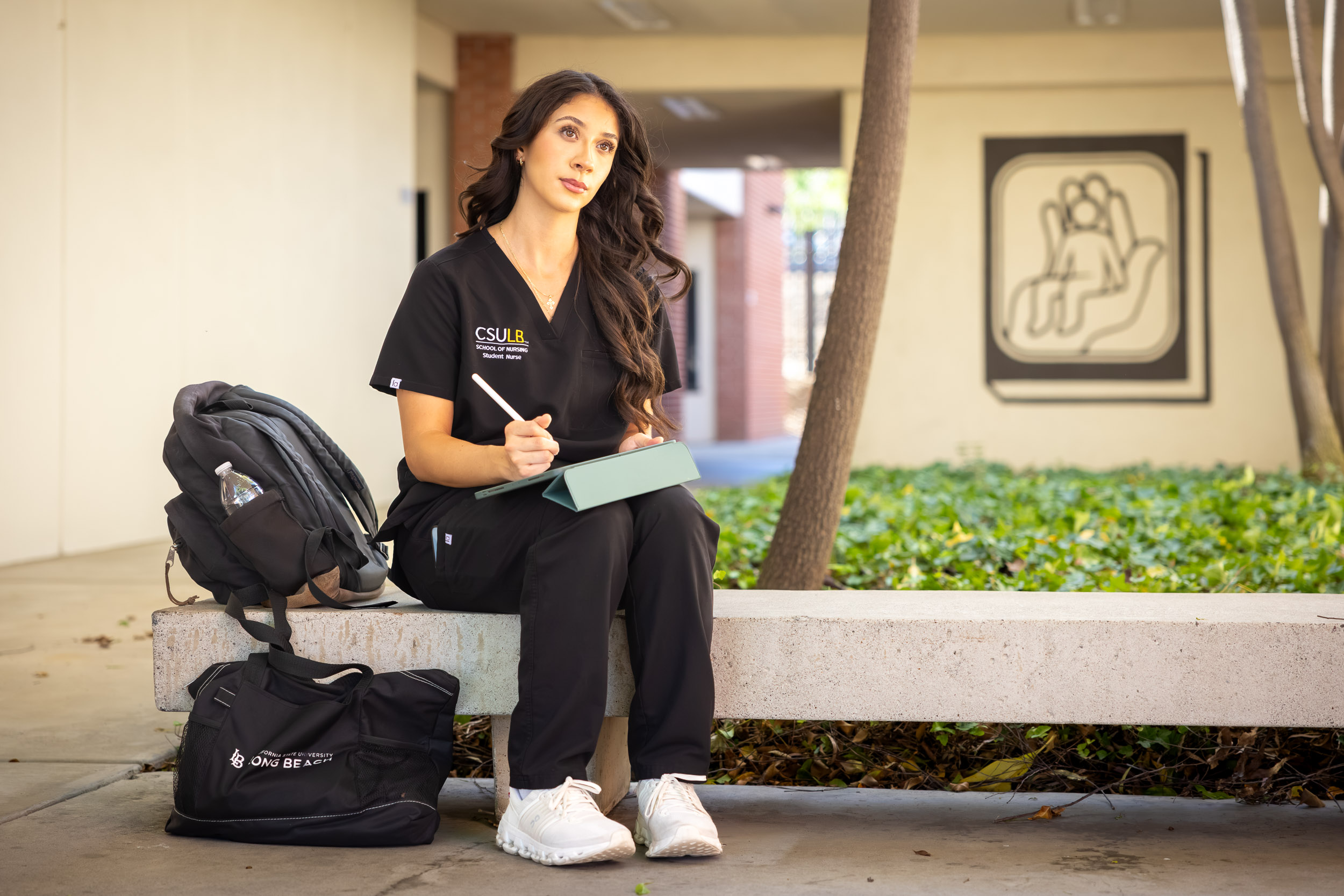 A person in scrubs sits on a bench with a tablet.