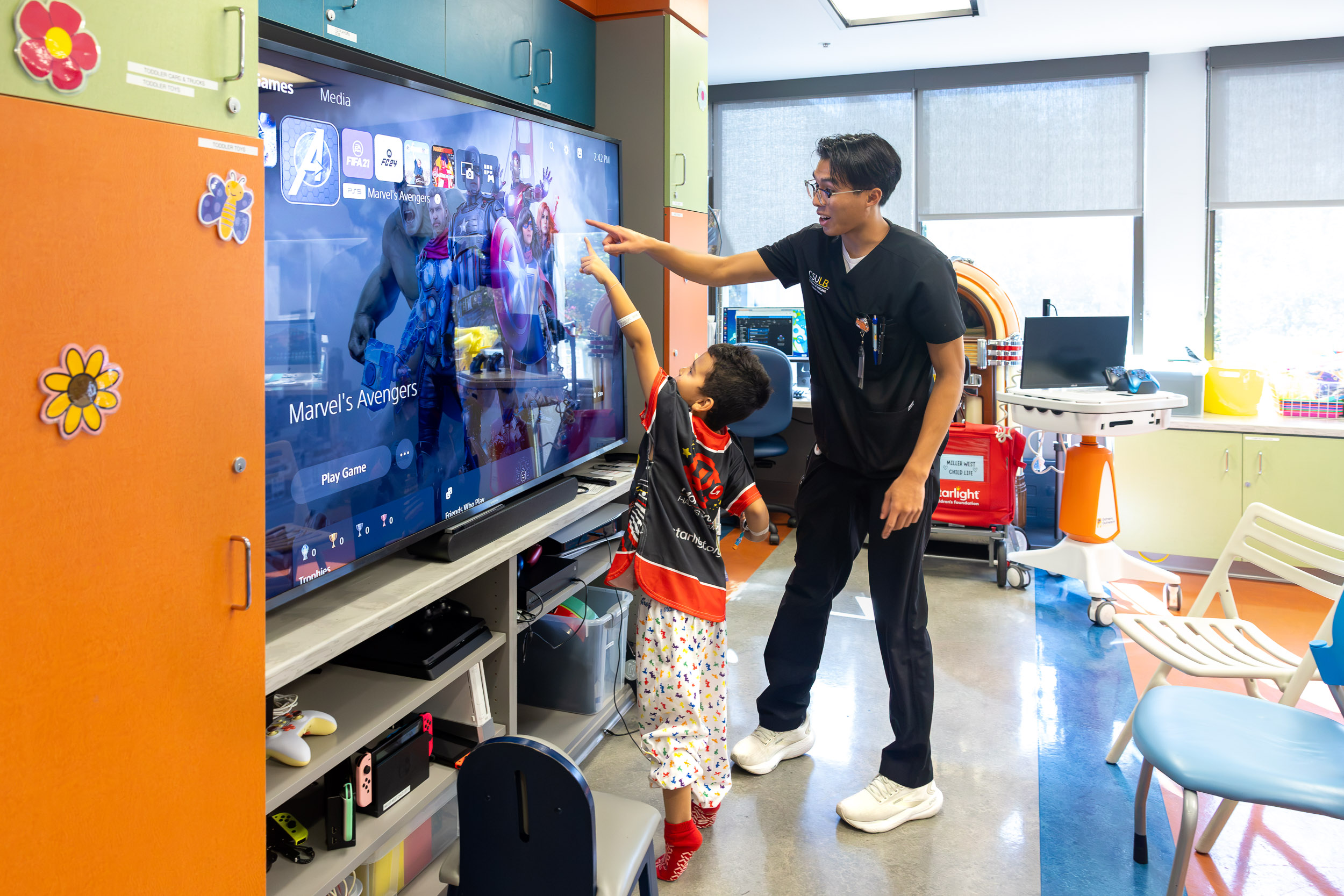 A person in scrubs and a young patient point at a video game screen.