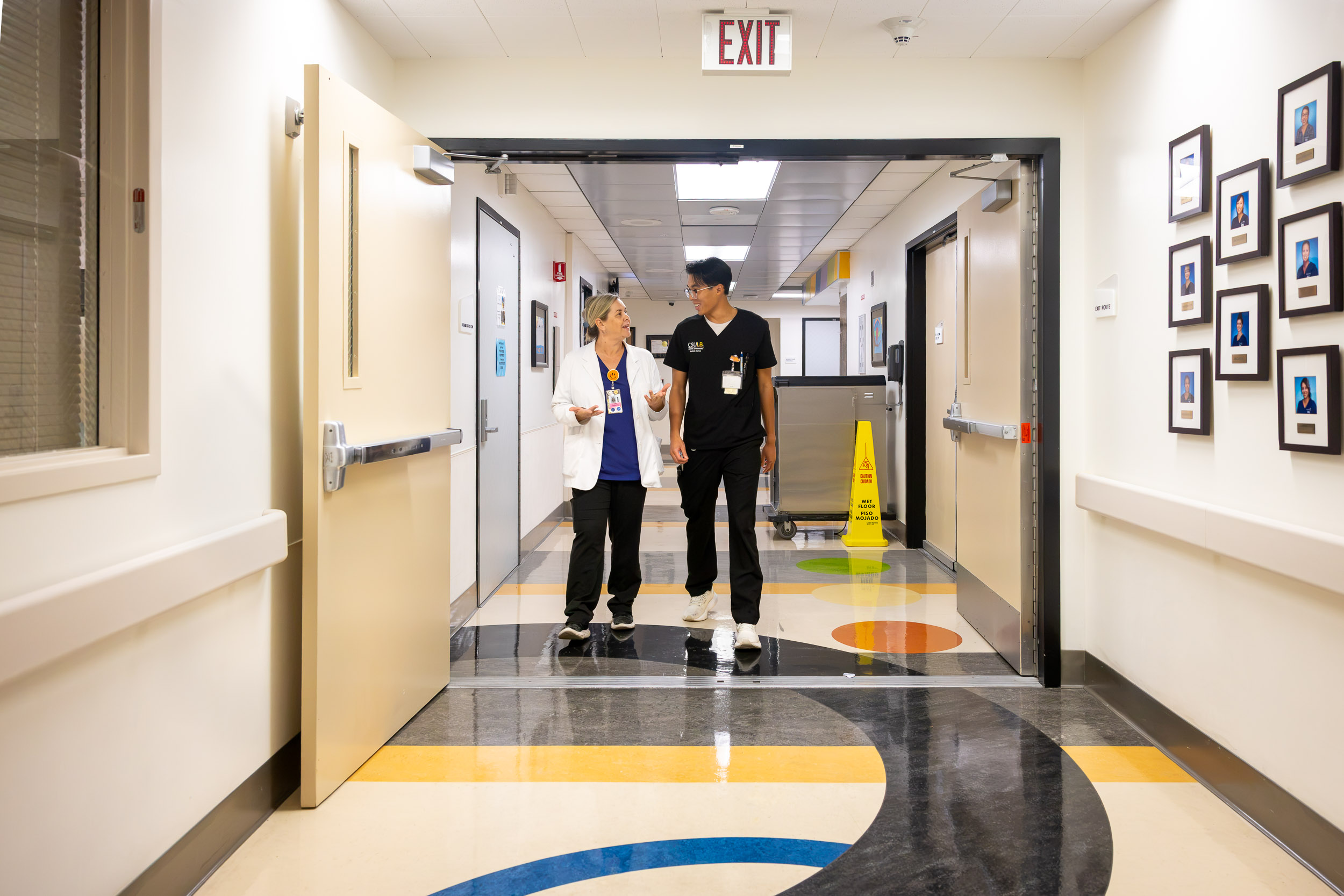 Two people talk as they walk down a hospital hallway.