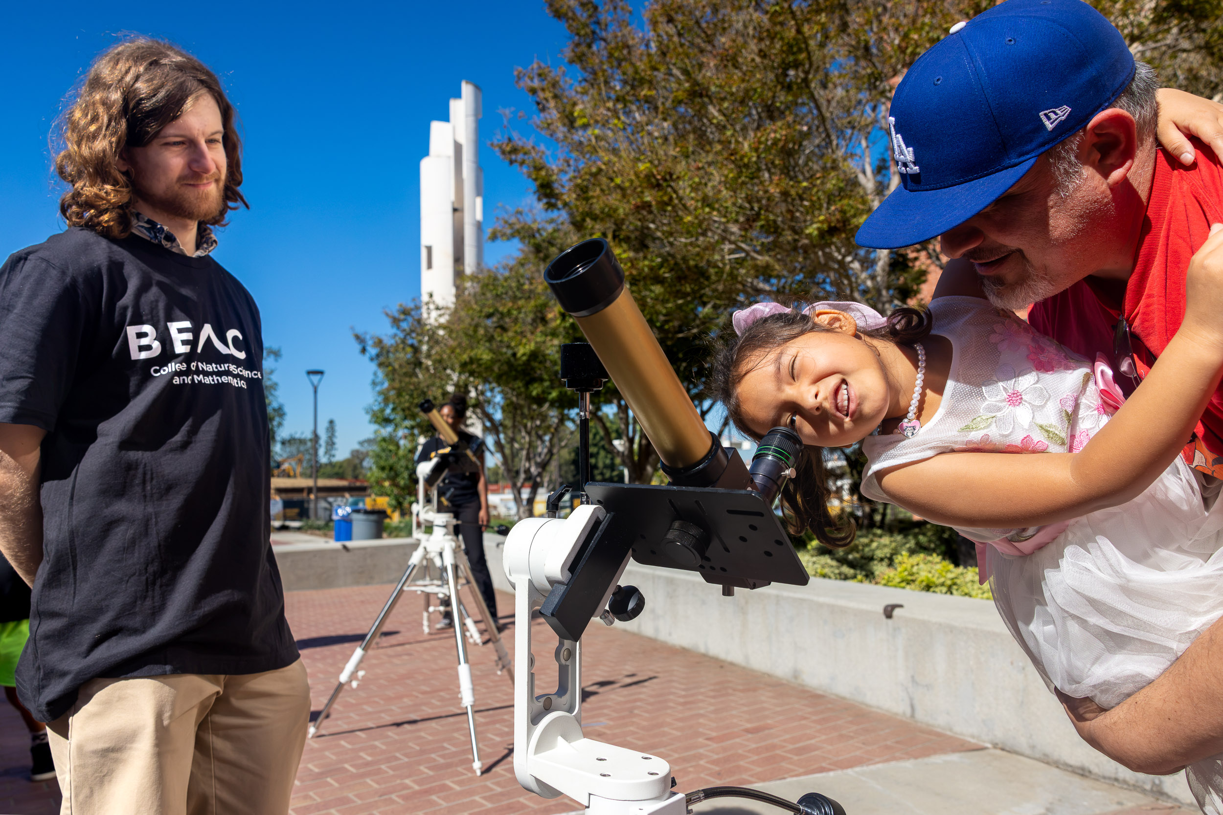 A child looks through a telescope as an adult holds her up.