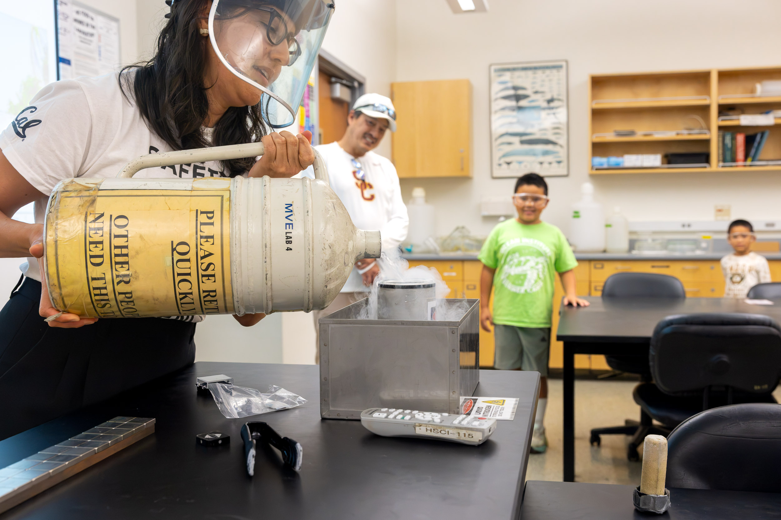 A person in a face shield pours liquid nitrogen as children watch.