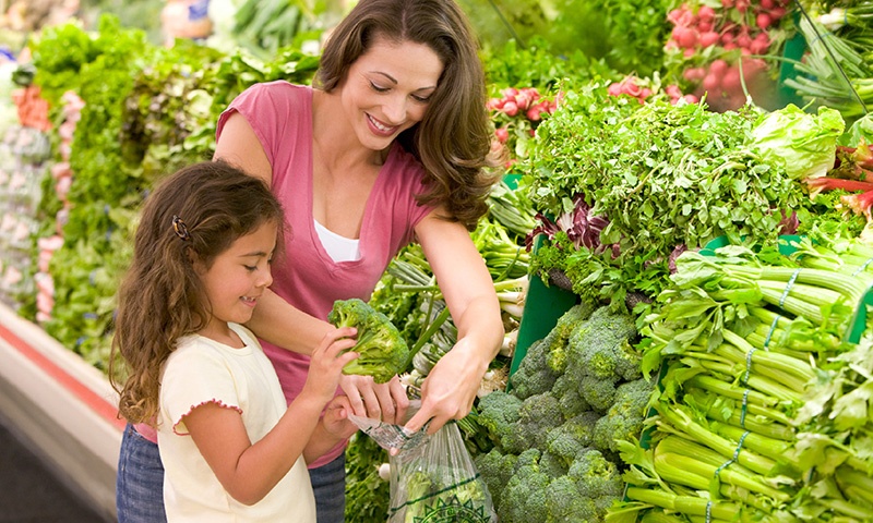 woman buying vegetables at grocery story with her daughter