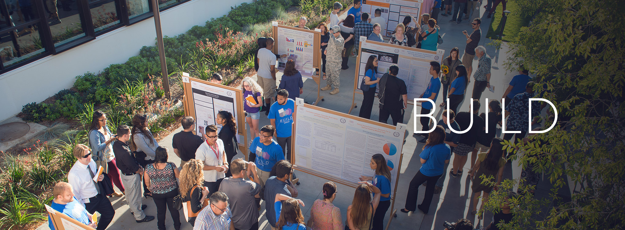 BUILD page banner depicting students at the Summer Symposium doing a poster session