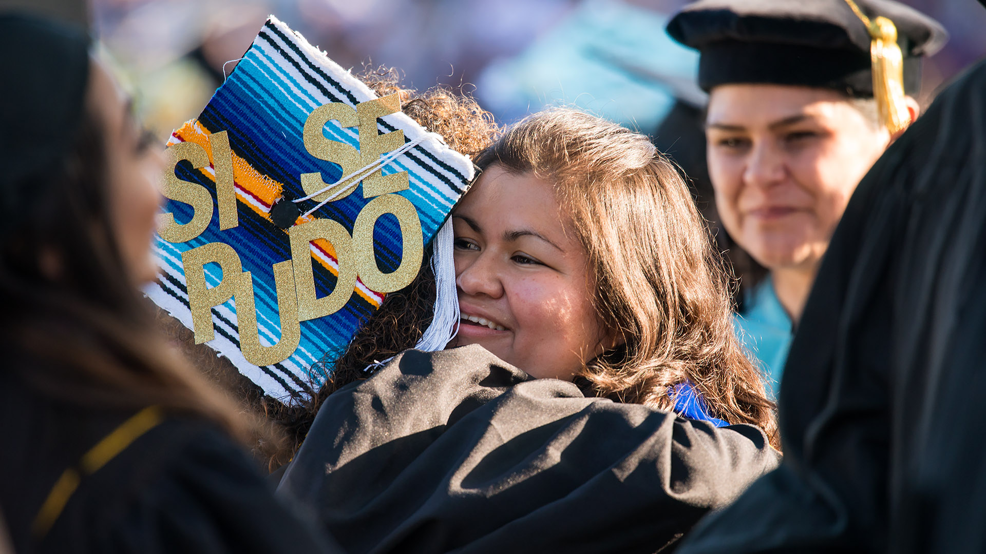 Latina students embrace a graduation.