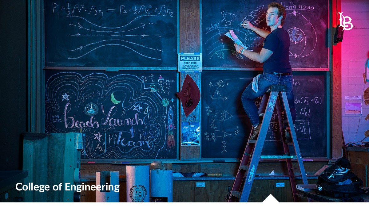 Student sitting atop ladder writing on chalkboard